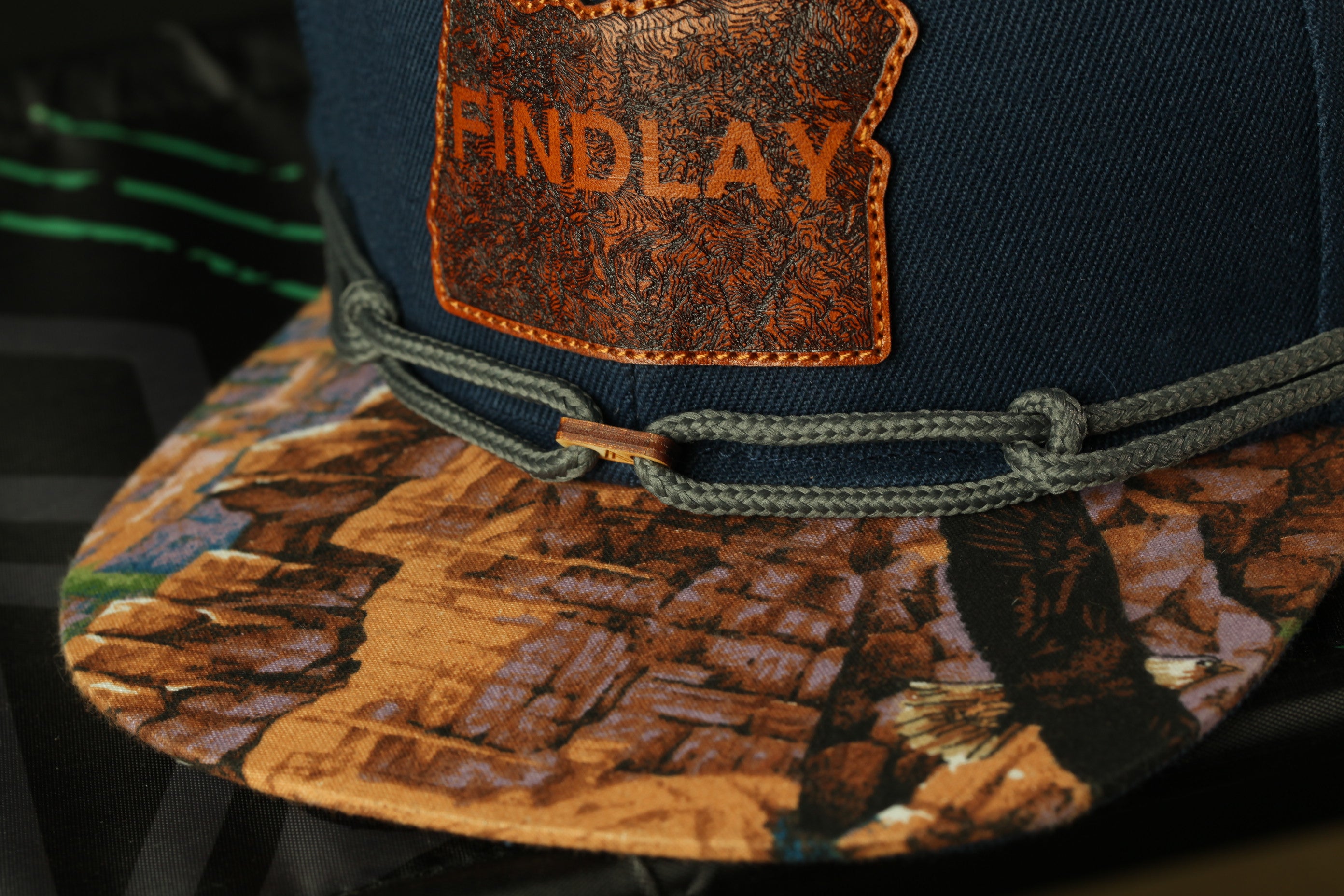 A close-up view of a dark blue baseball cap with a printed design on the front and a leather patch on the side.