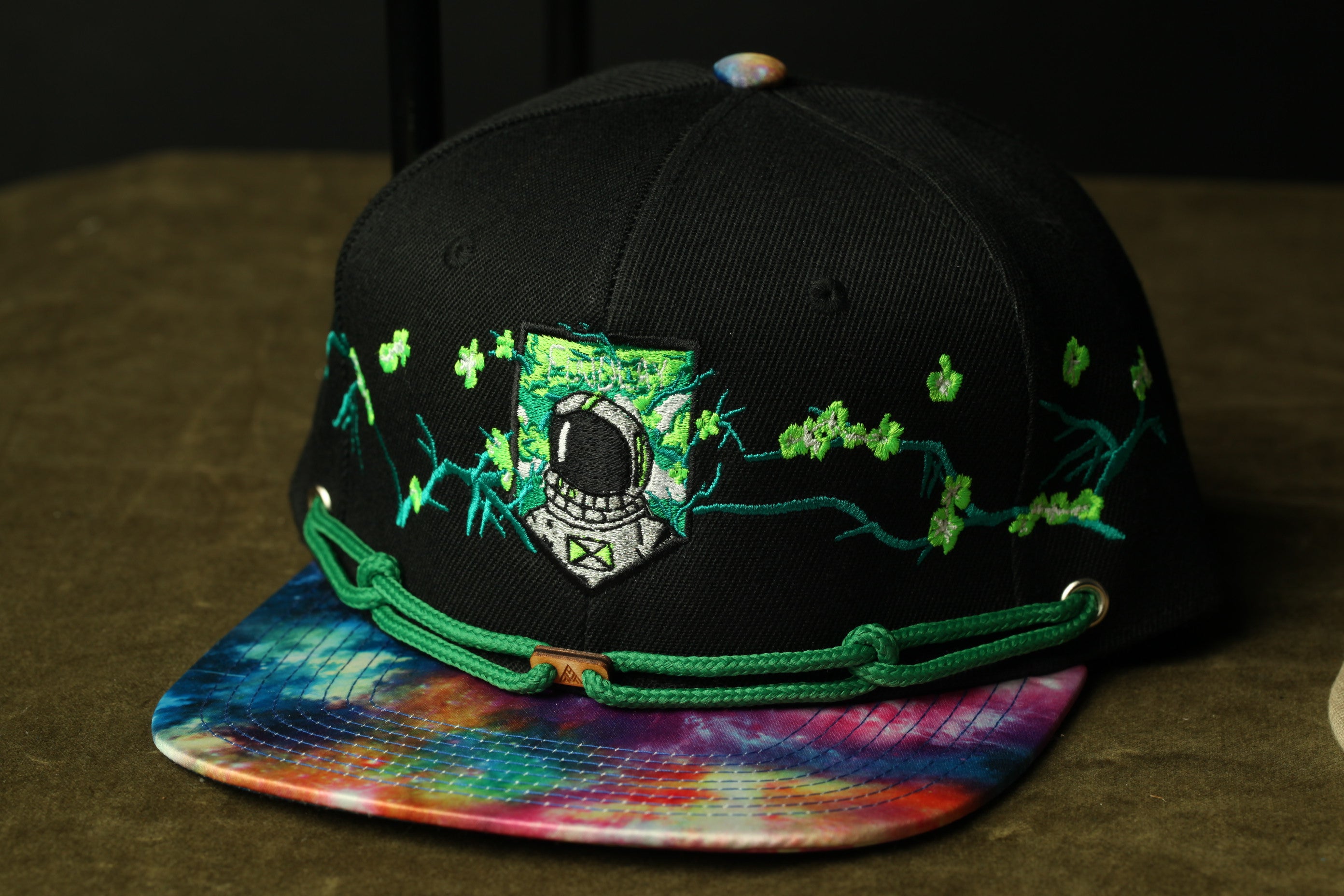 A black baseball cap with a tie-dye pattern and a small emblem on the front, placed on a table.