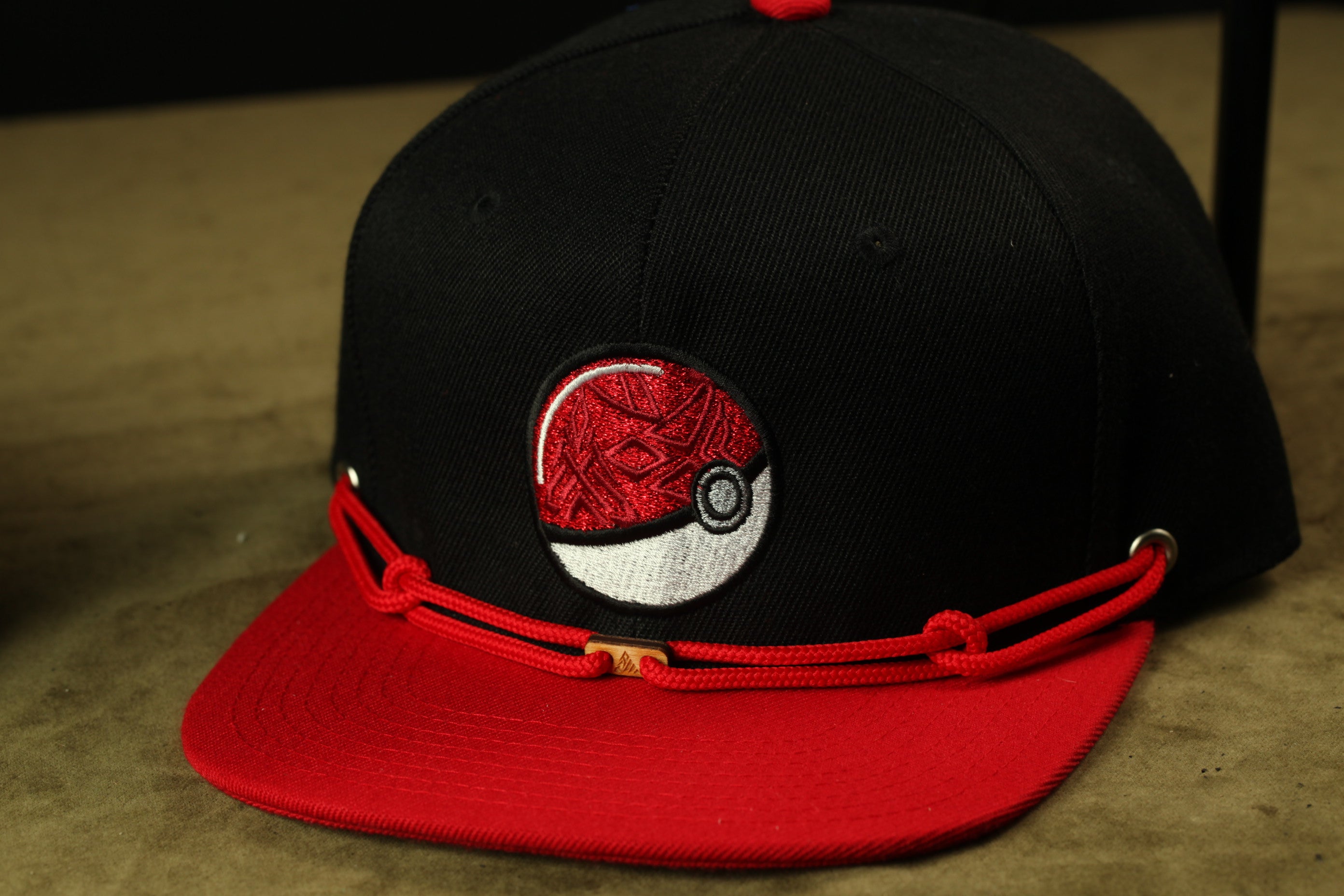 A black baseball cap with a red brim and a red and white Pokemon ball embroidered on the front.