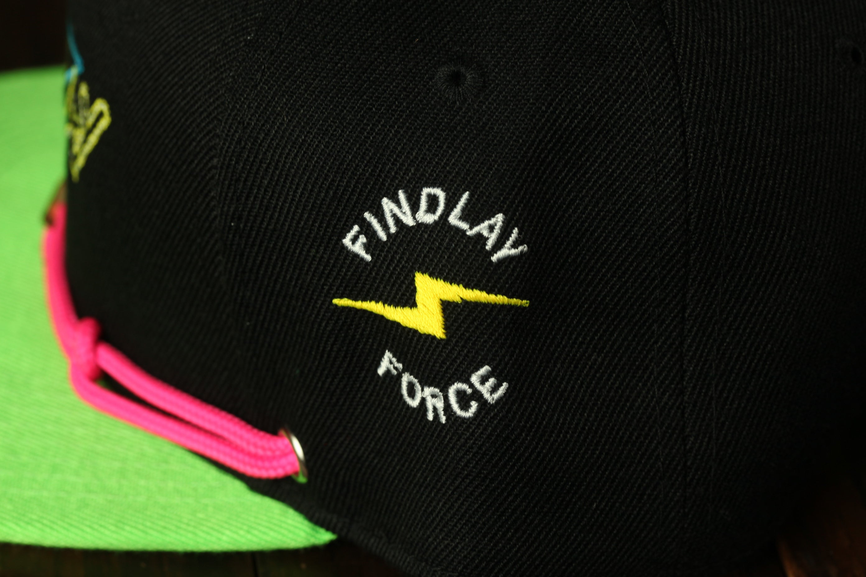 A close-up view of a black baseball cap with a yellow lightning bolt symbol and the text "FINDLAY FORCE" embroidered on it.