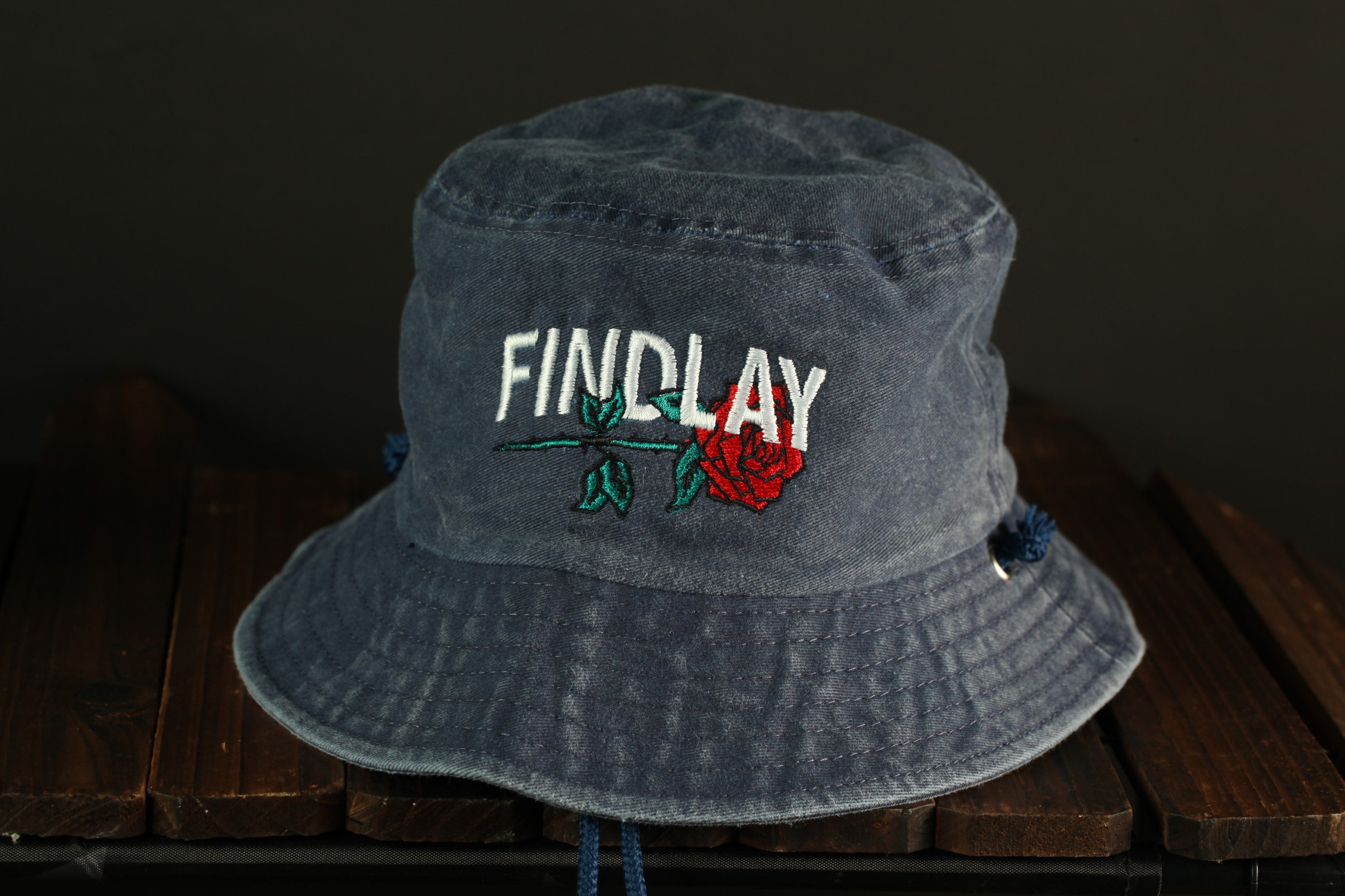 A gray bucket hat with the word "FINDlay" embroidered on it, sitting on a wooden surface.