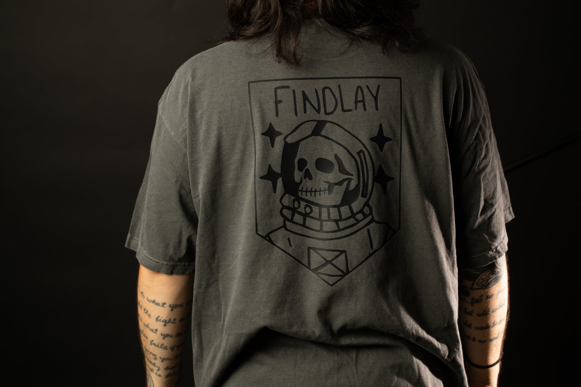 the back of a person wearing a gray t-shirt with a graphic design featuring a skull wearing a spacesuit.