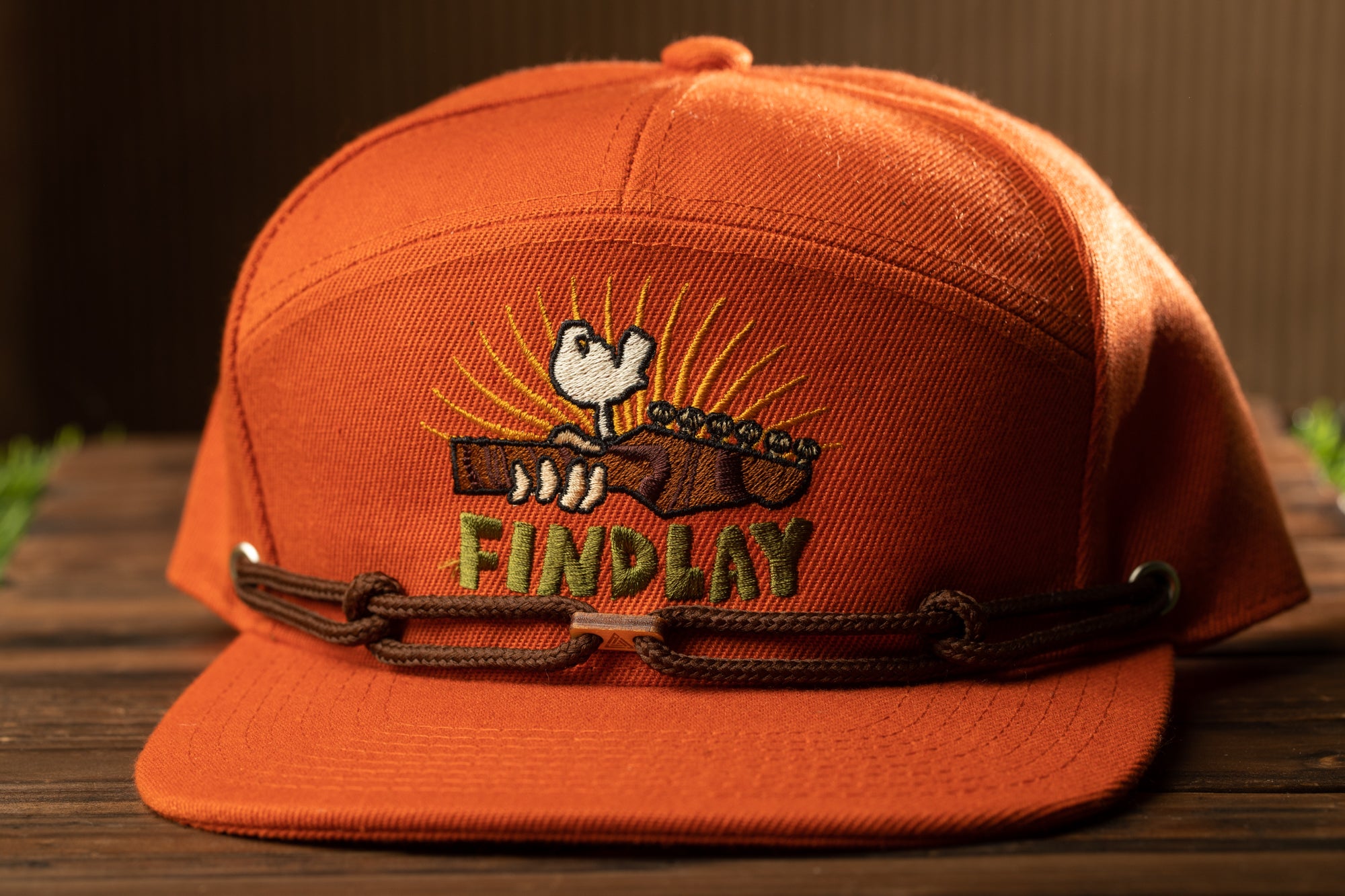 An orange baseball cap with an embroidered design on the front, featuring a cartoon character and the text "FINDlay".
