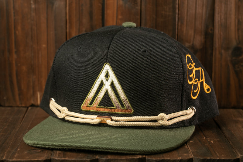 A black baseball cap with a green brim and a white triangle logo on the front, placed on a wooden surface.