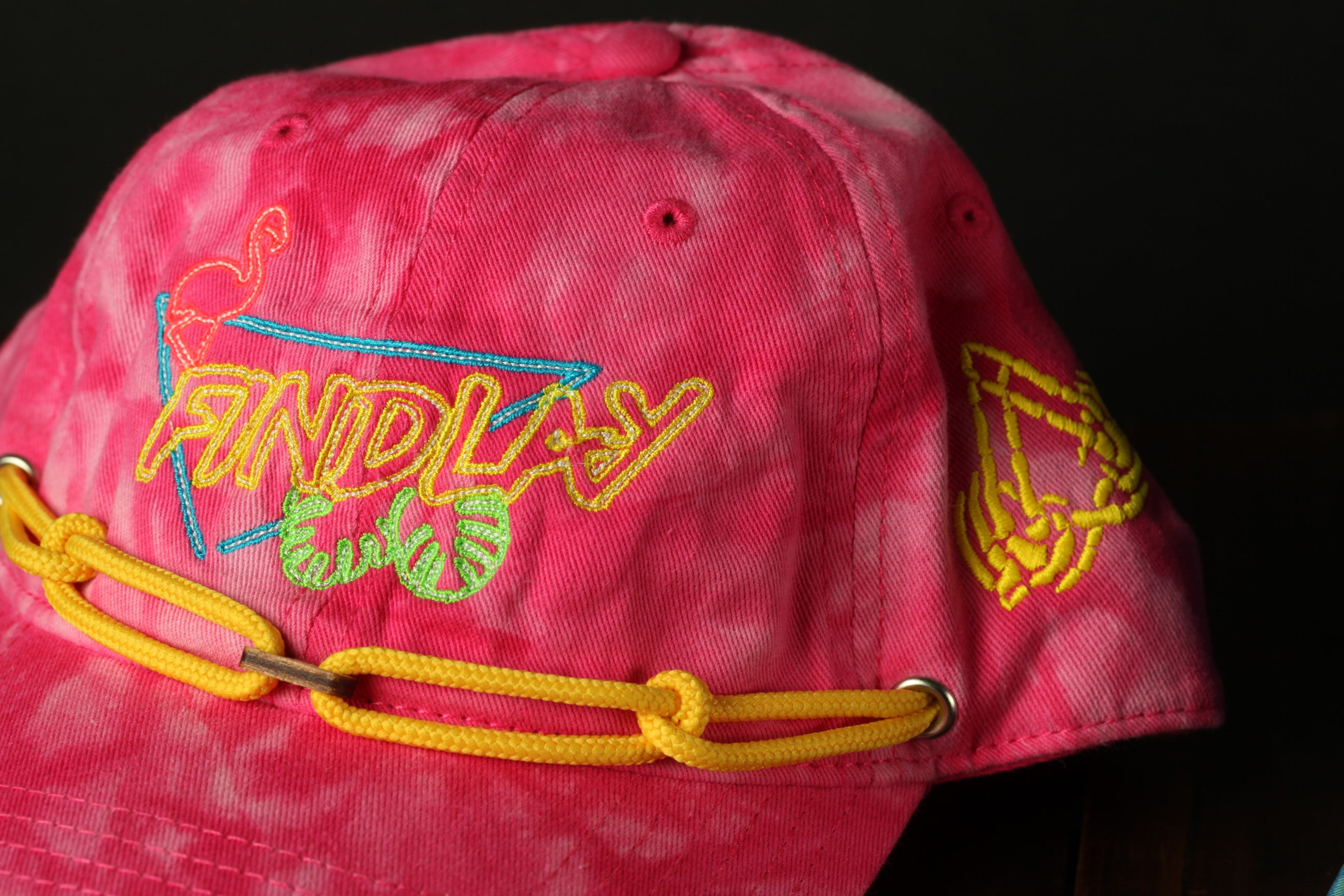 A close-up of a pink tie-dye baseball cap with yellow and blue embroidered designs.