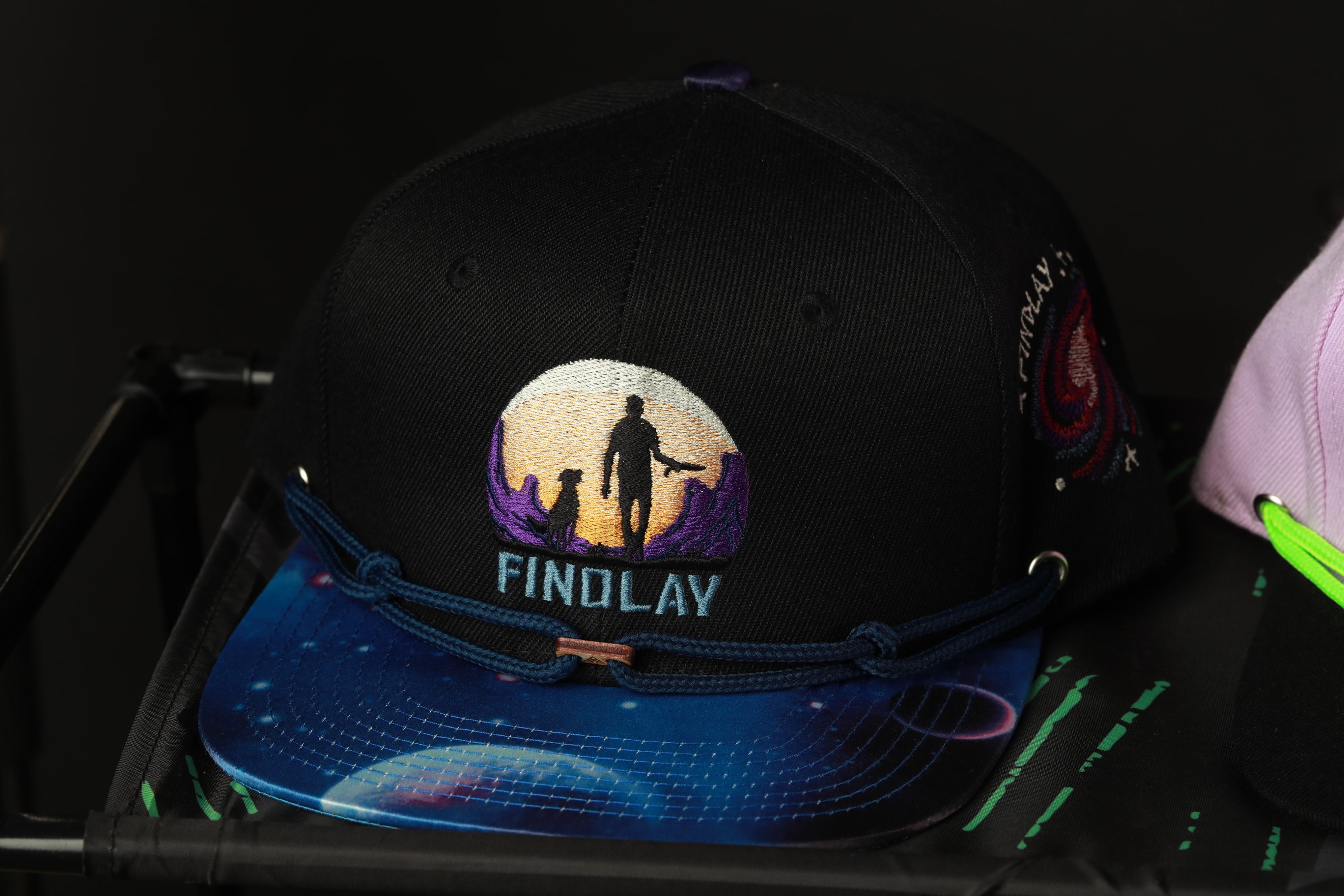 A black baseball cap with a colorful, space-themed design and the word "FINDLAY" printed on it.