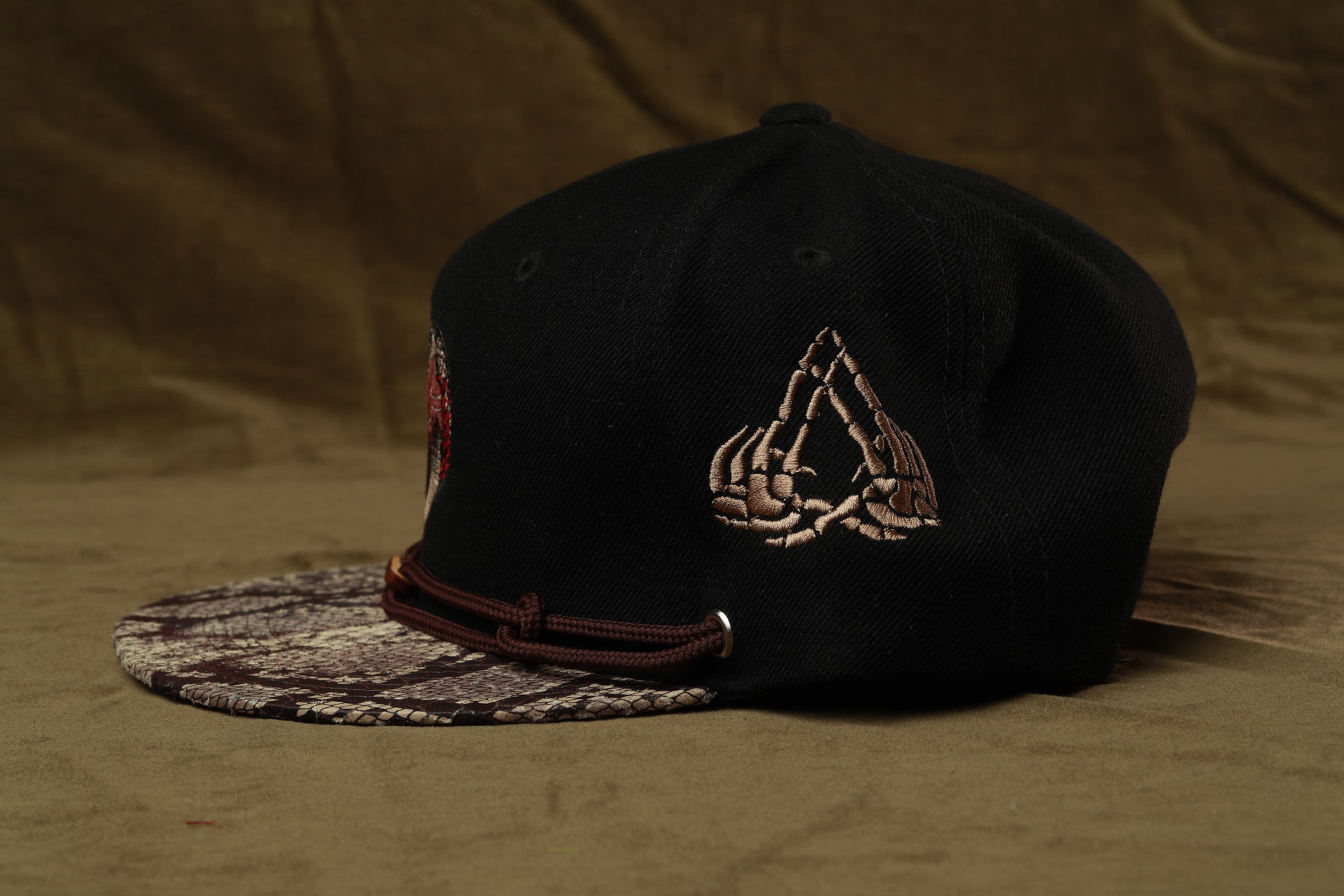 A black baseball cap with a unique design on the front, featuring a skeleton hand and a geometric pattern.