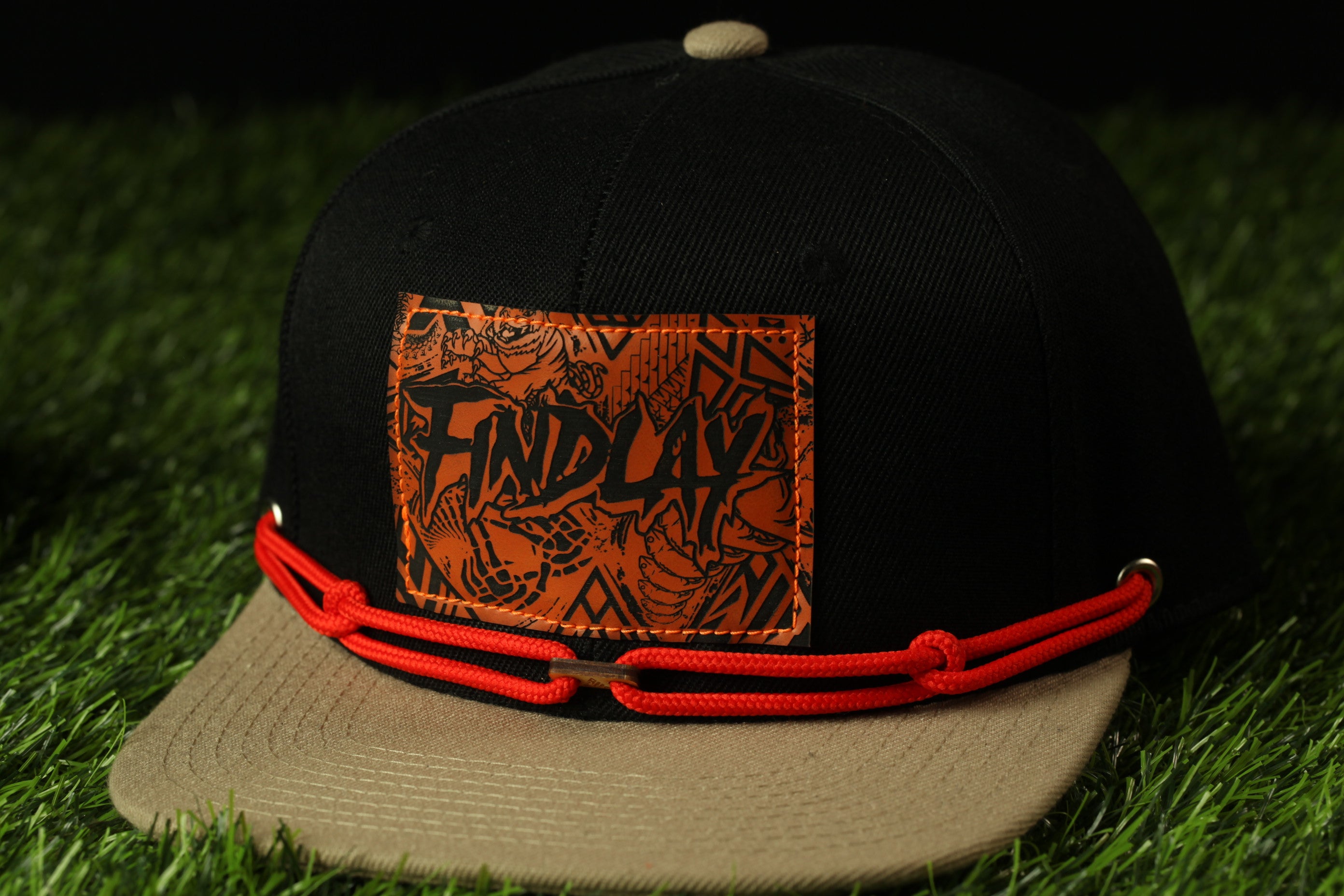 A black baseball cap with a red string and a patch on the front displaying the word "FINDlay".