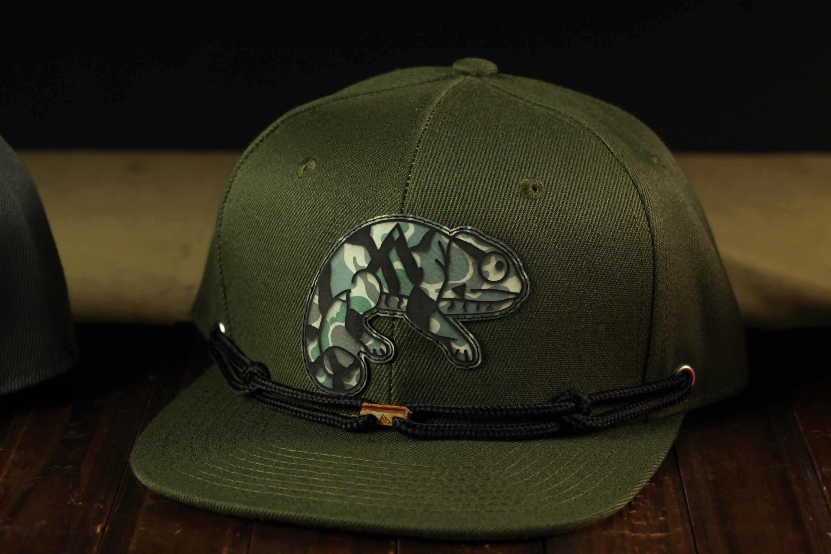 A green baseball cap with a camouflage pattern and a small animal design on the front.
