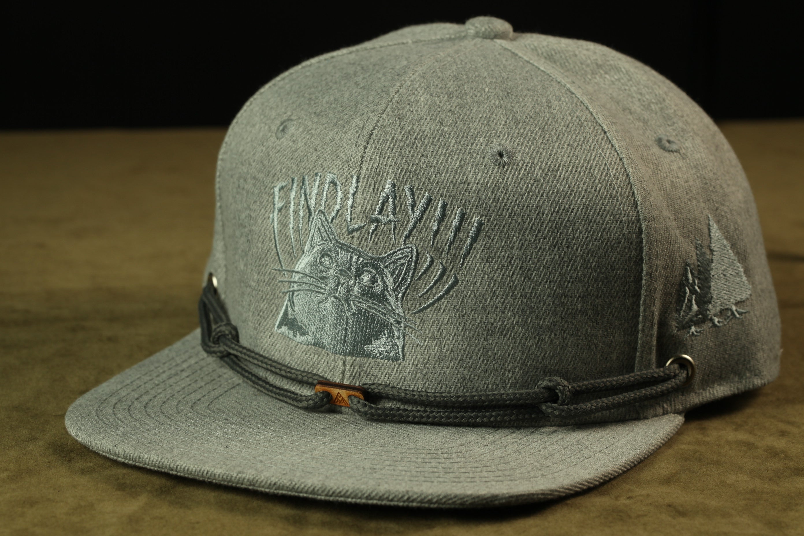 A gray baseball cap with a cat embroidered on it, sitting on a brown surface.