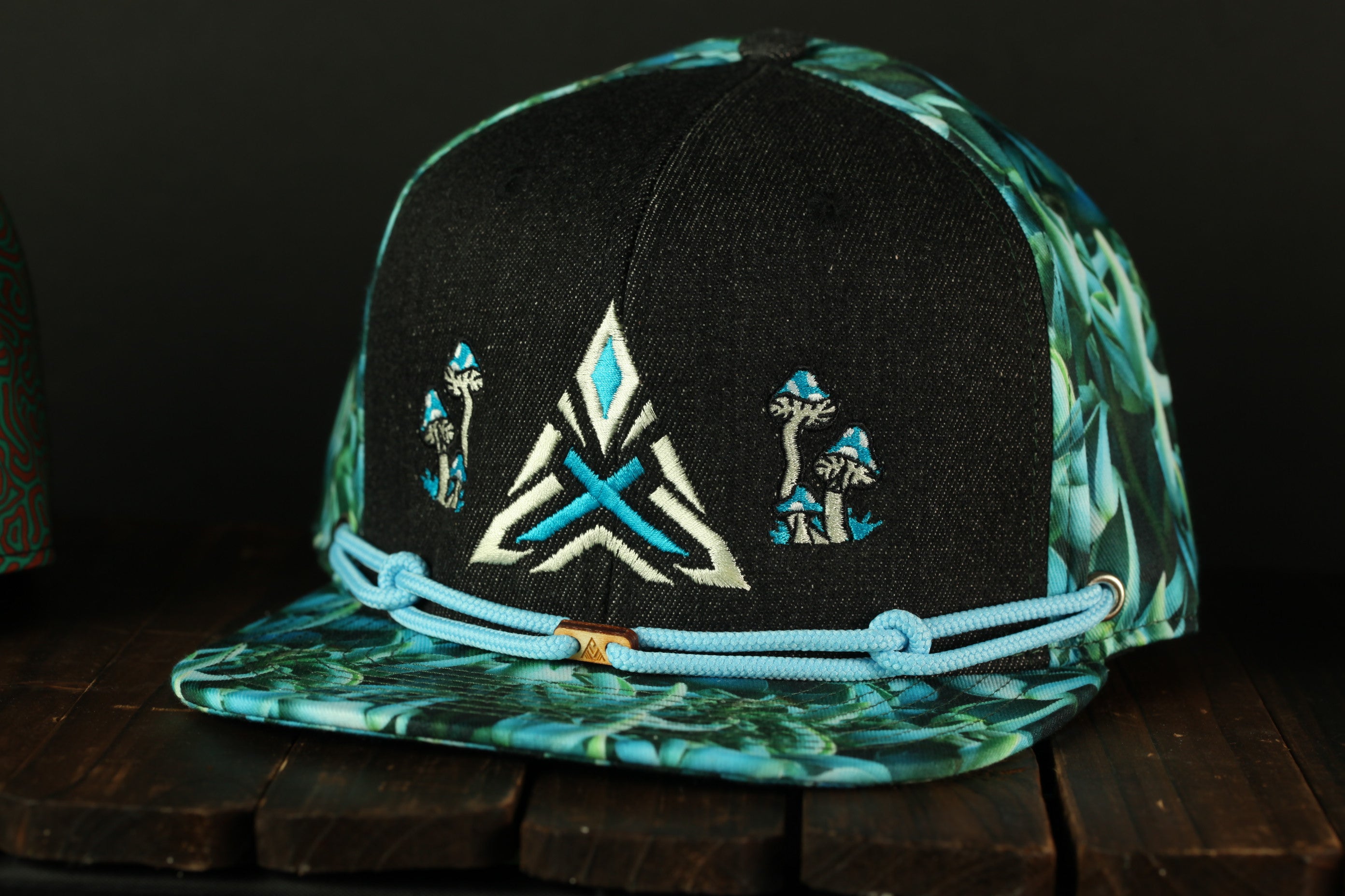 A black baseball cap with a floral pattern and a geometric design on the front, sitting on a wooden surface.