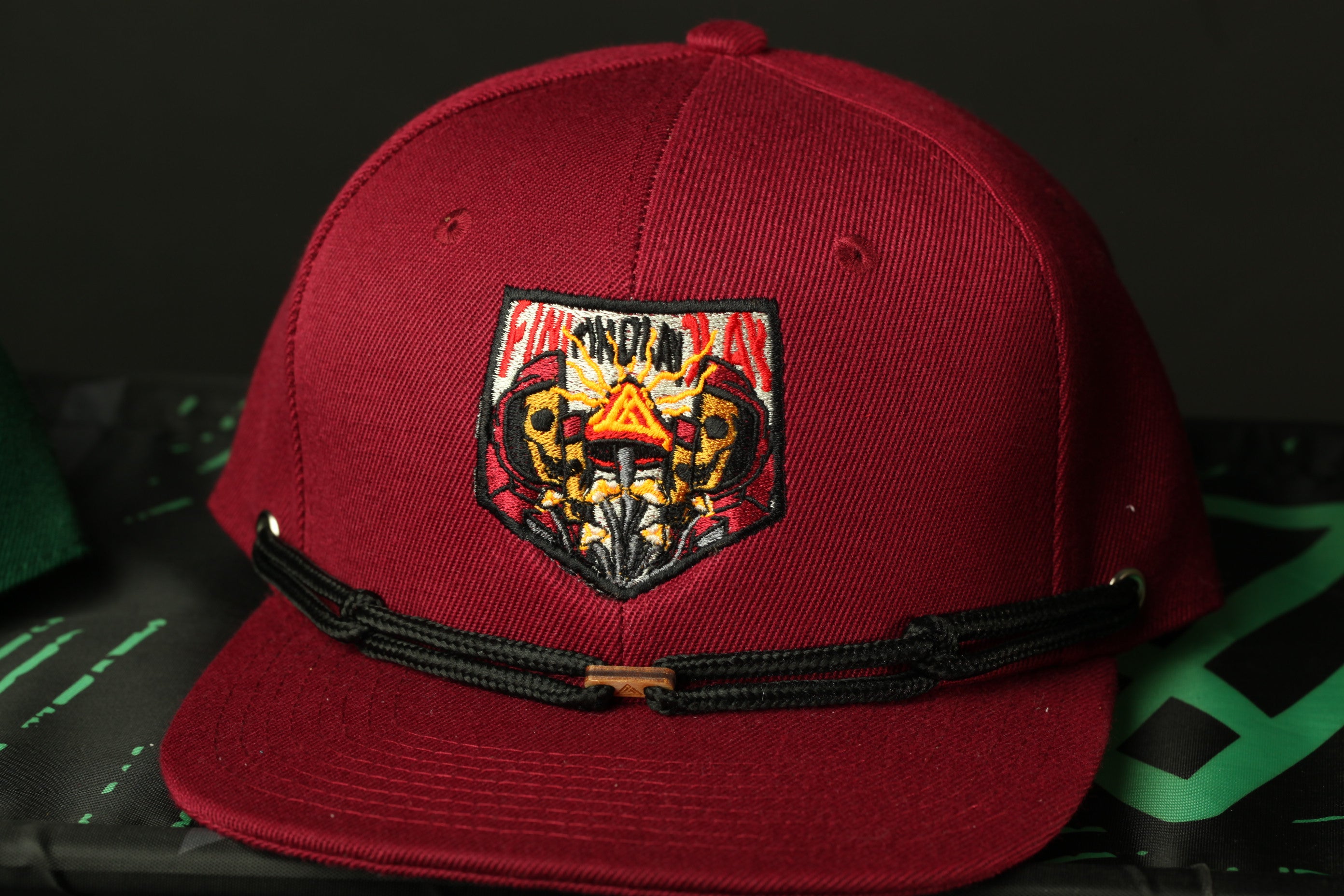 A maroon baseball cap with a black adjustable strap and a patch on the front.