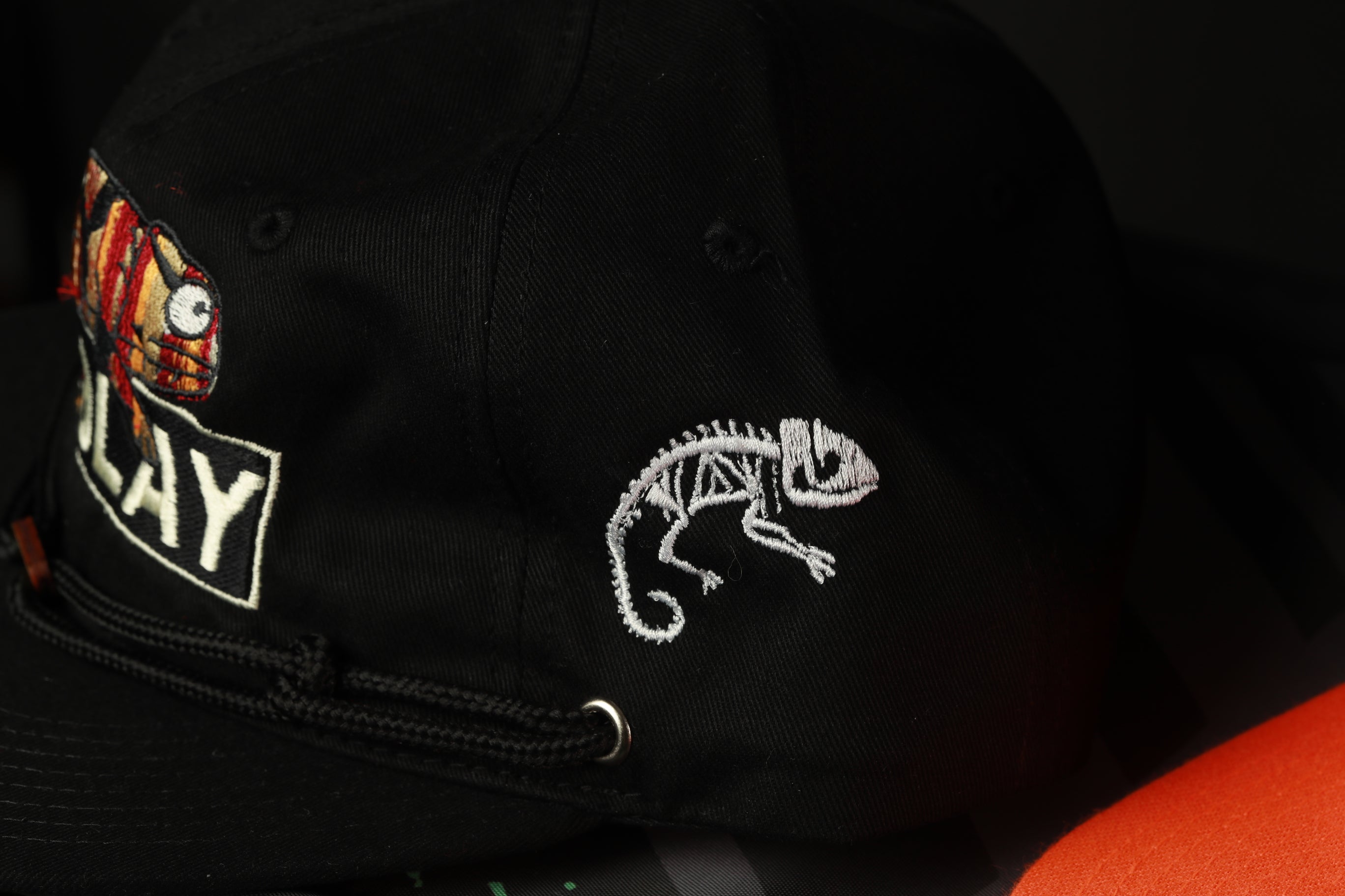 A close-up view of a black baseball cap with a chameleon embroidered on it.