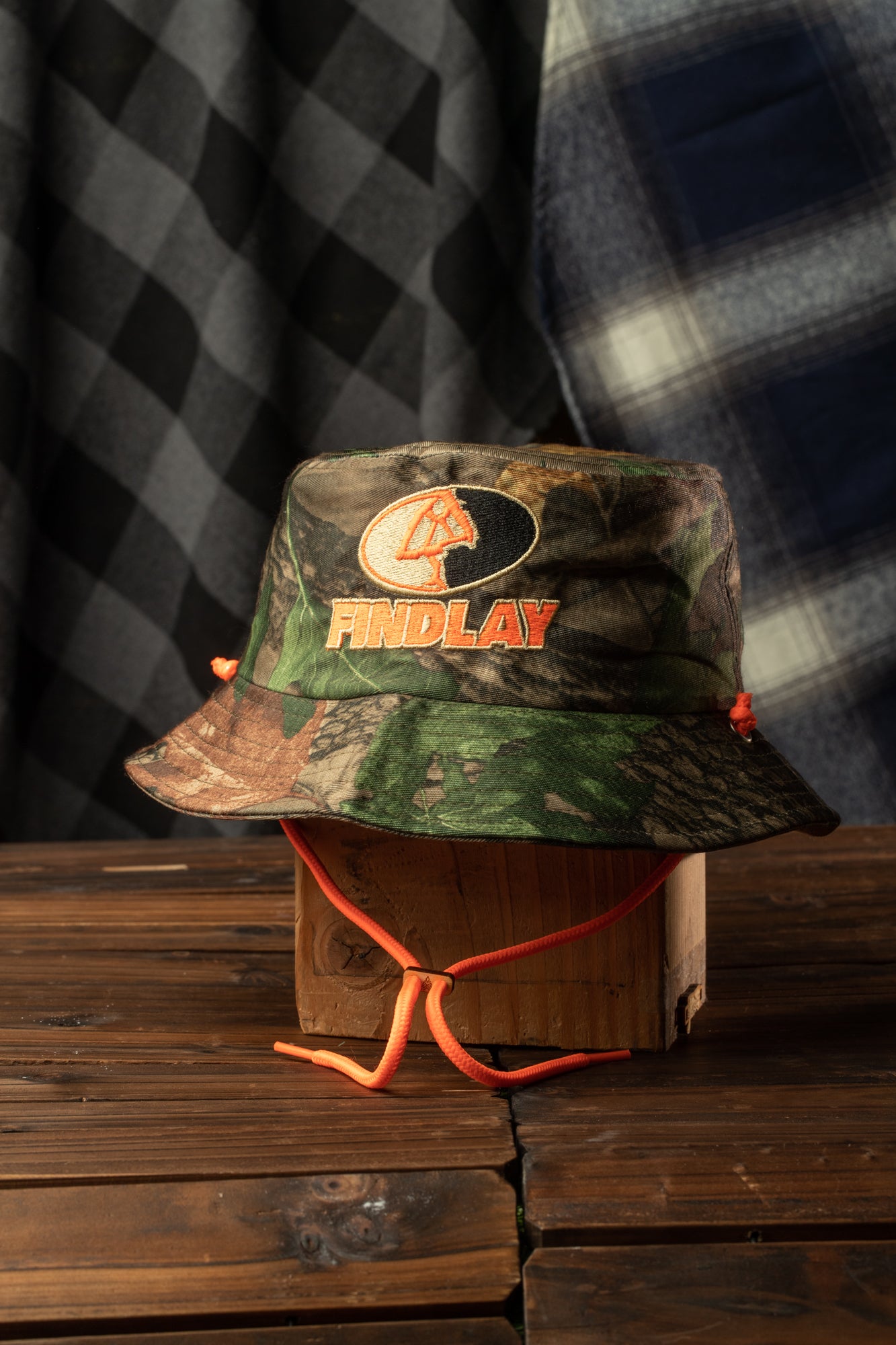 A camouflage bucket hat with the word "Findlay" printed on it, placed on a wooden surface.