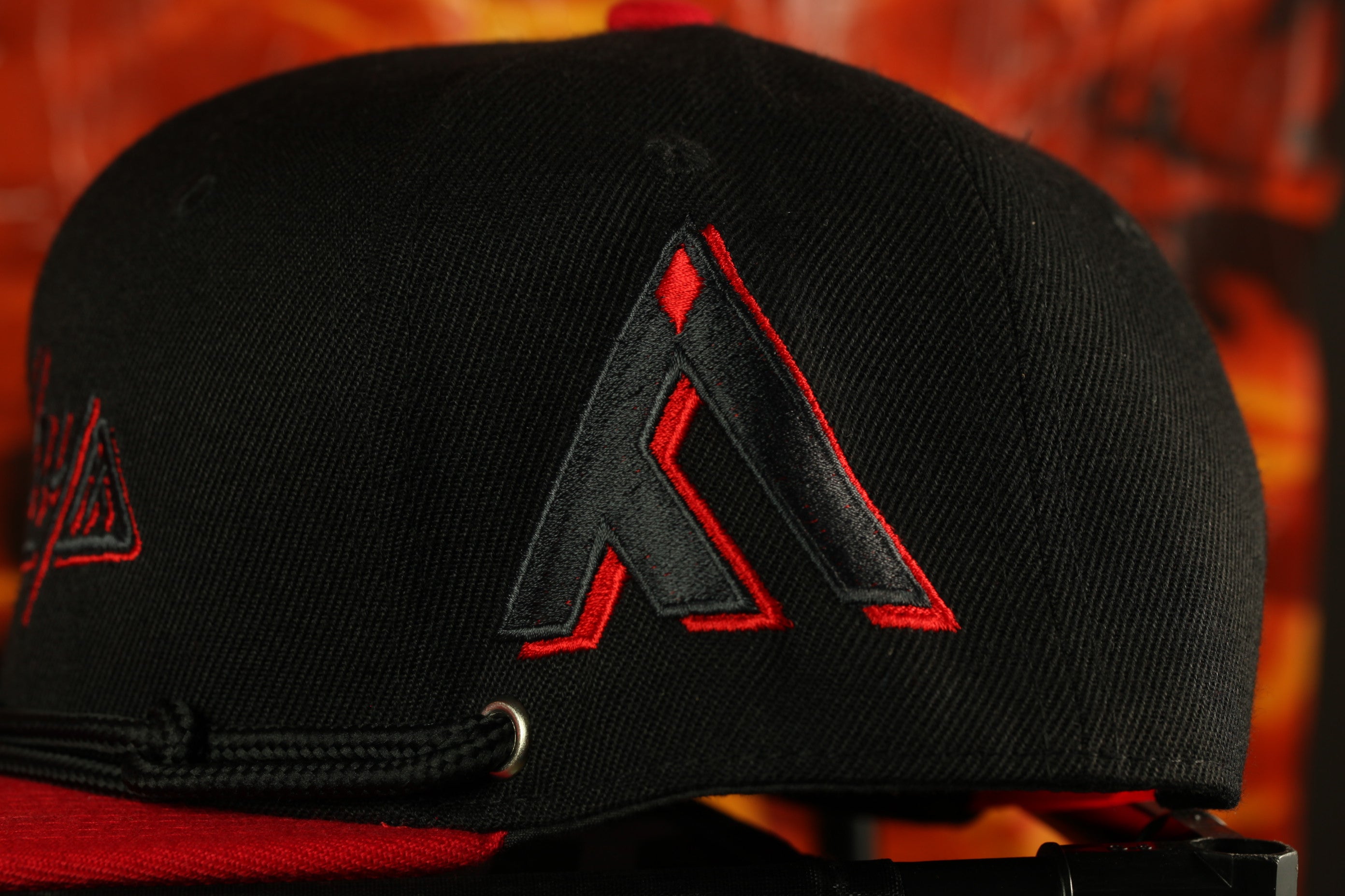 A close-up view of a black baseball cap with a red logo on it.