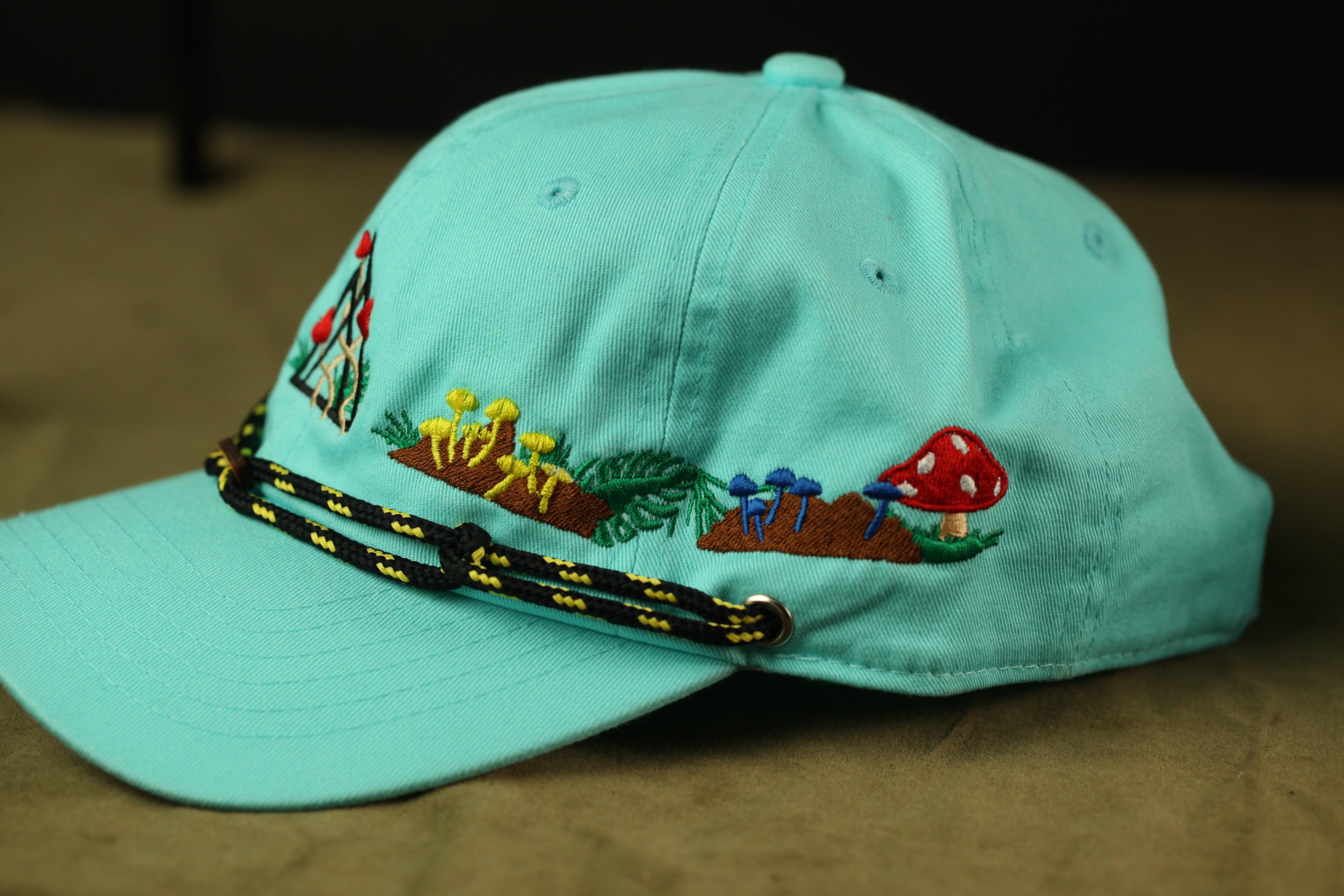 A turquoise baseball cap with colorful mushroom and leaf designs on the front.