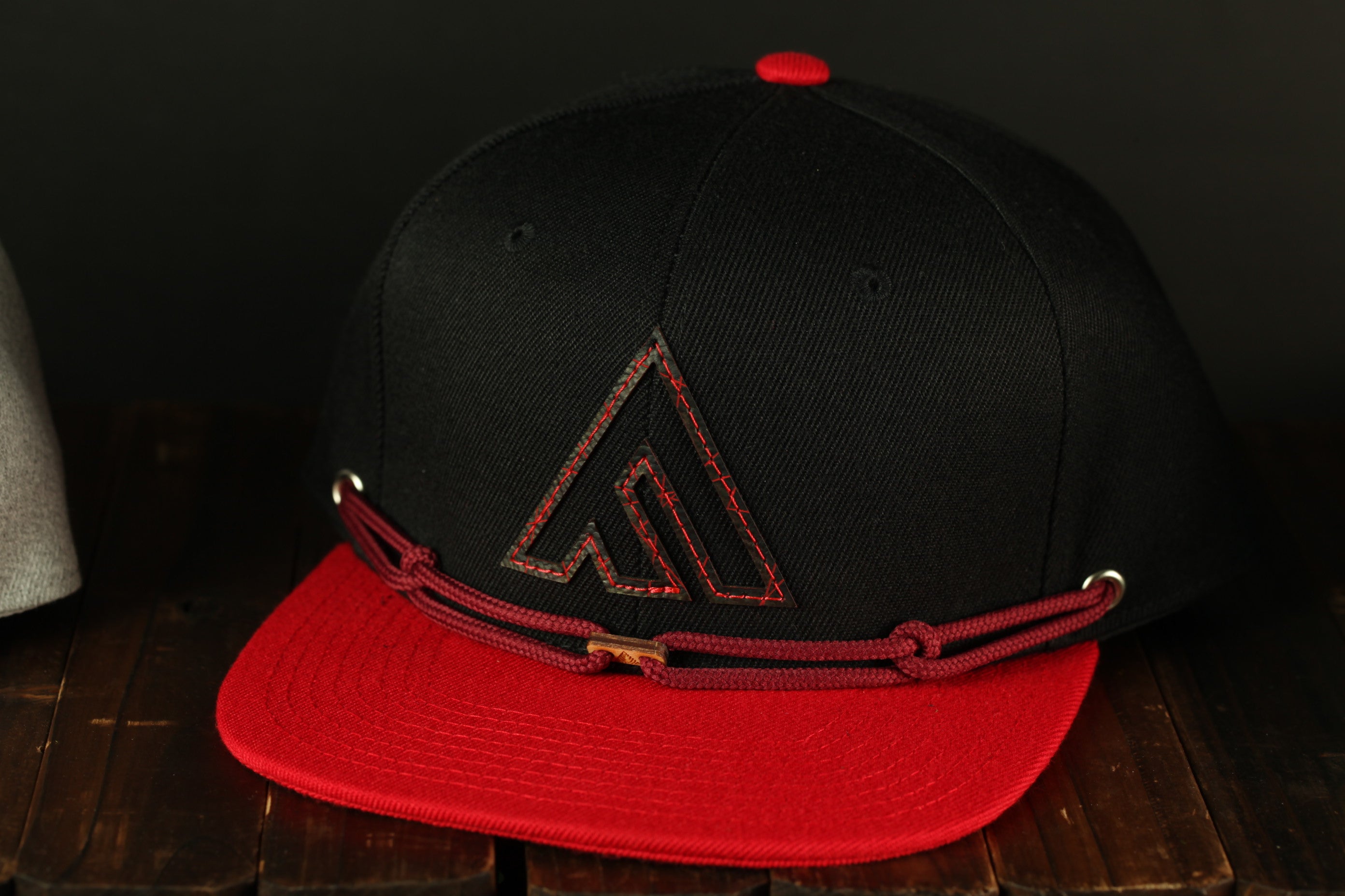 A black baseball cap with a red brim and a red logo on the front, placed on a wooden surface.