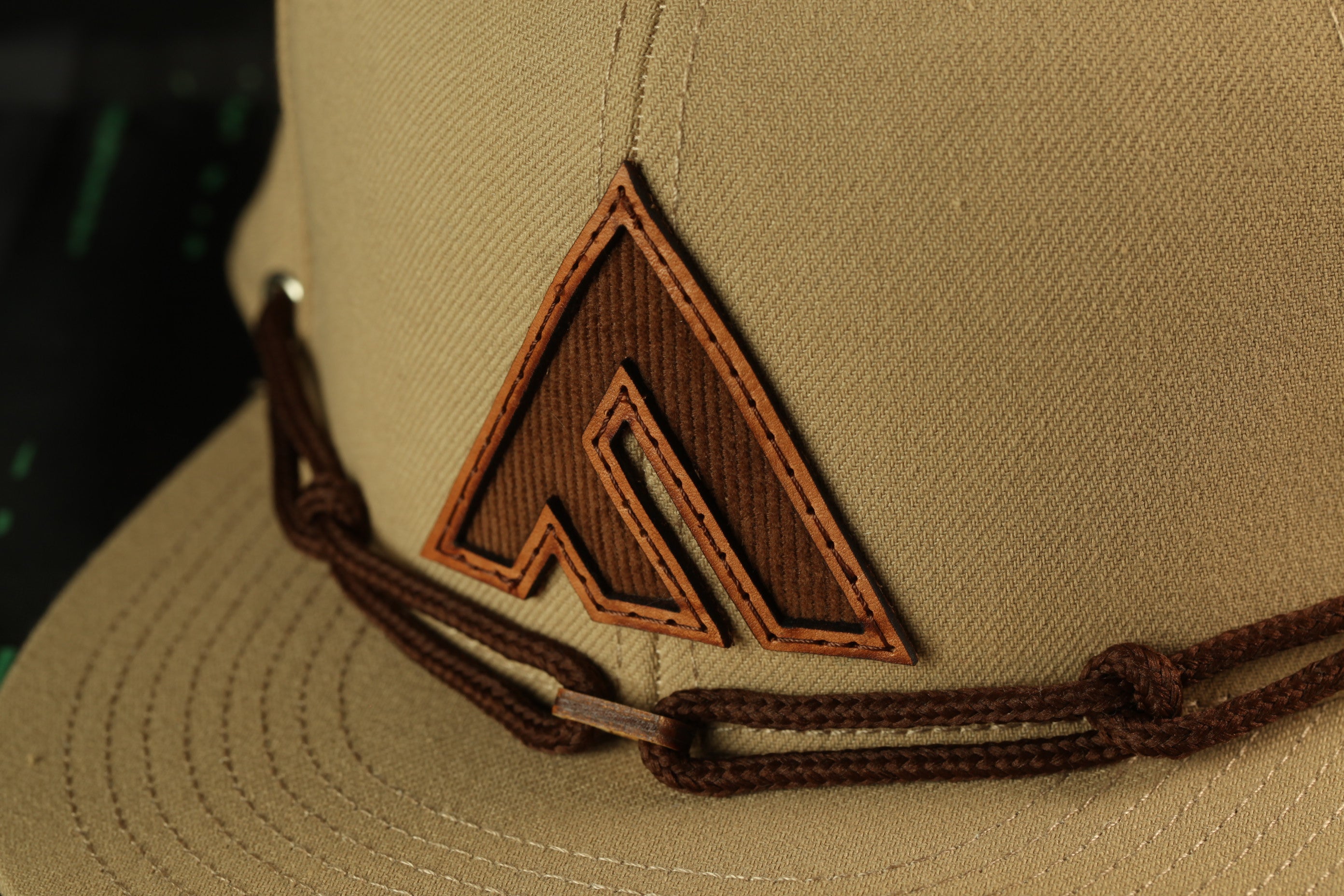 A close-up view of a beige baseball cap with a brown leather logo on the front.
