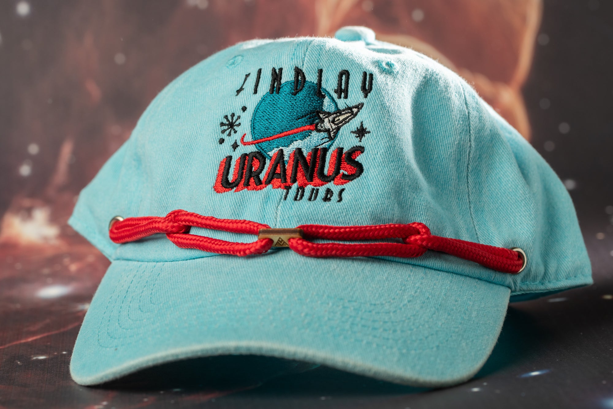 A light blue baseball cap with a red string and a logo on it, featuring the text "INDLAY URANUS" and "2000" on it.