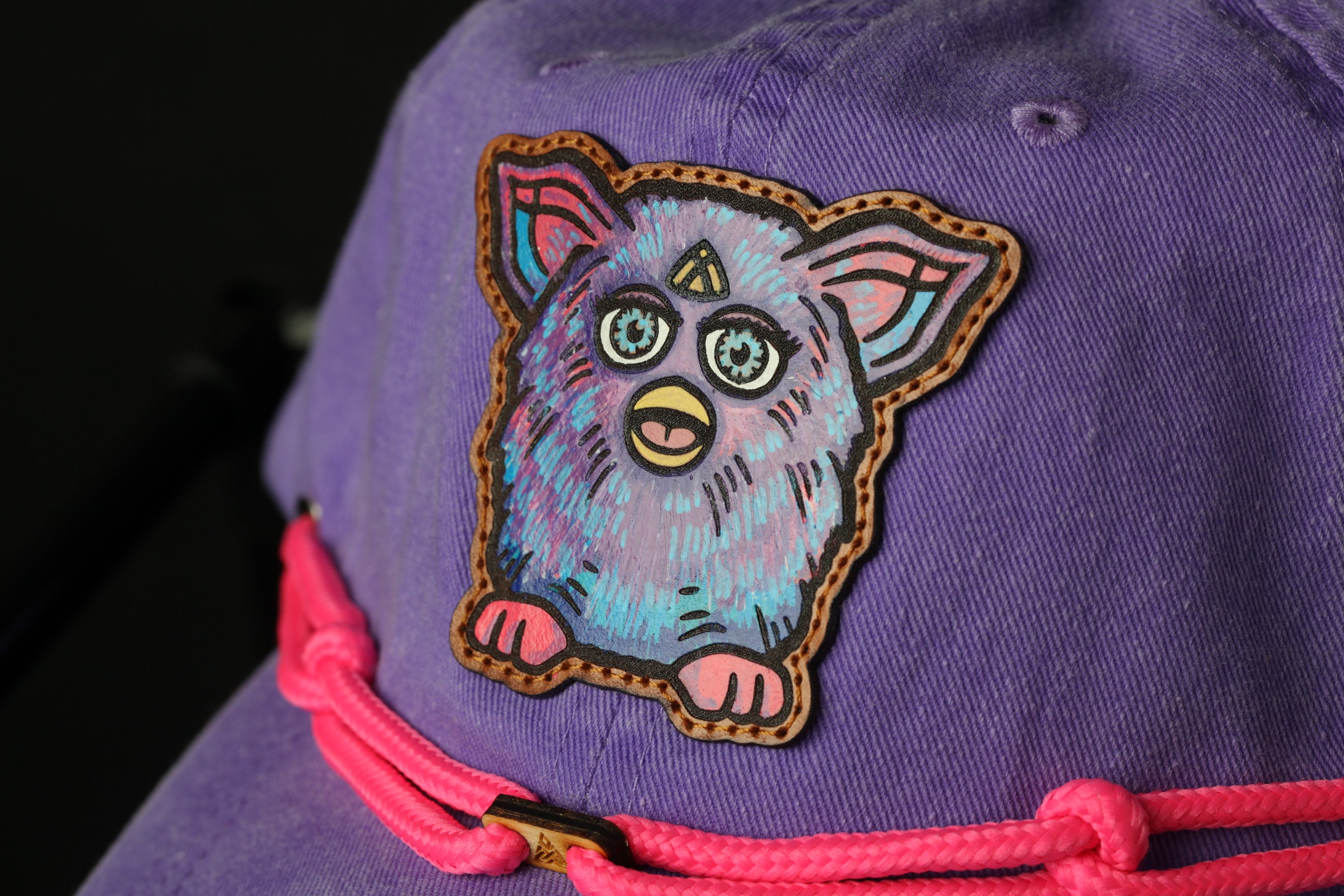 A close-up view of a purple baseball cap with a cartoon-style teddy bear patch on the front.