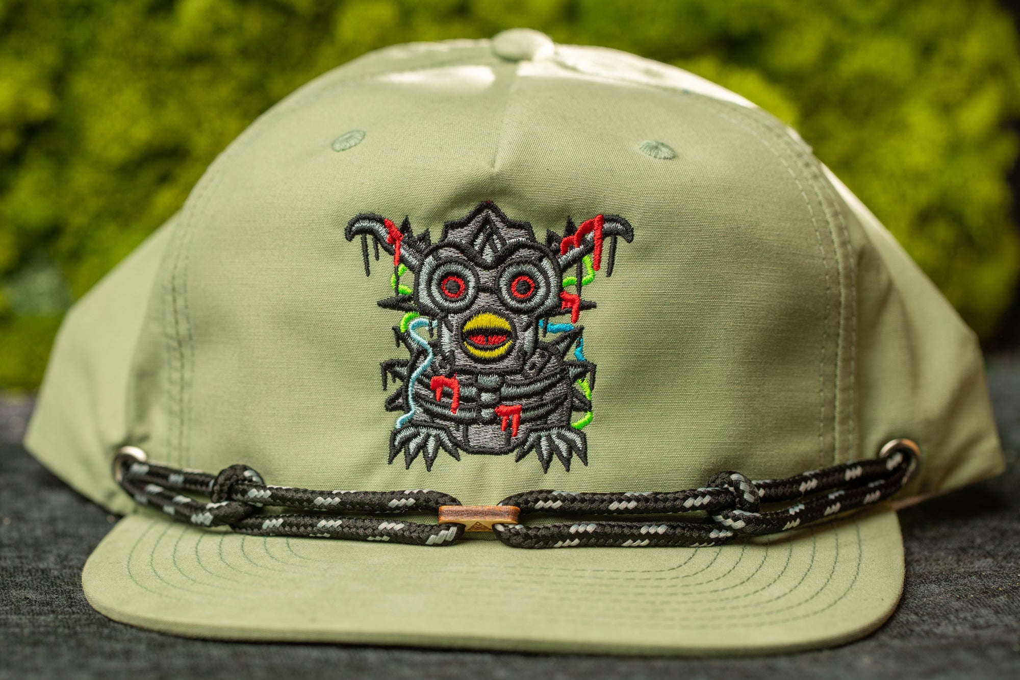 A green baseball cap with a unique embroidered design featuring a cartoon-like creature with red eyes and a yellow body.