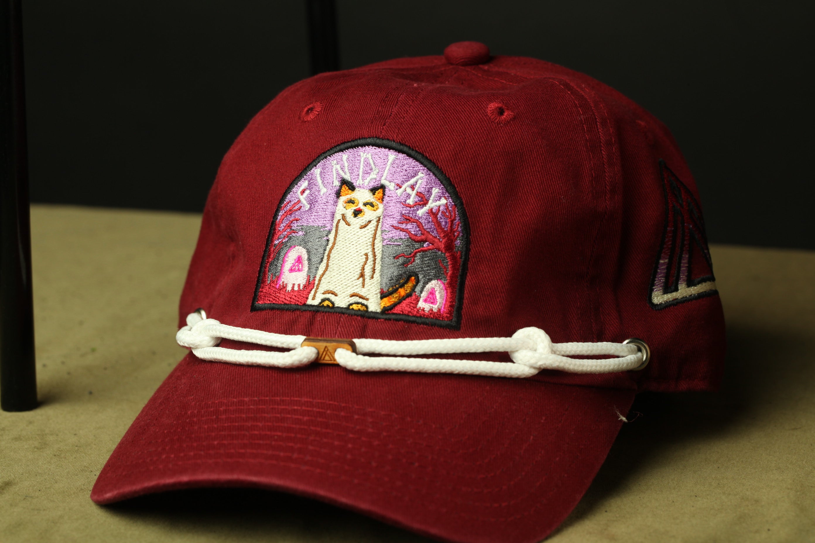 A red baseball cap with a cat embroidered on it, sitting on a surface.