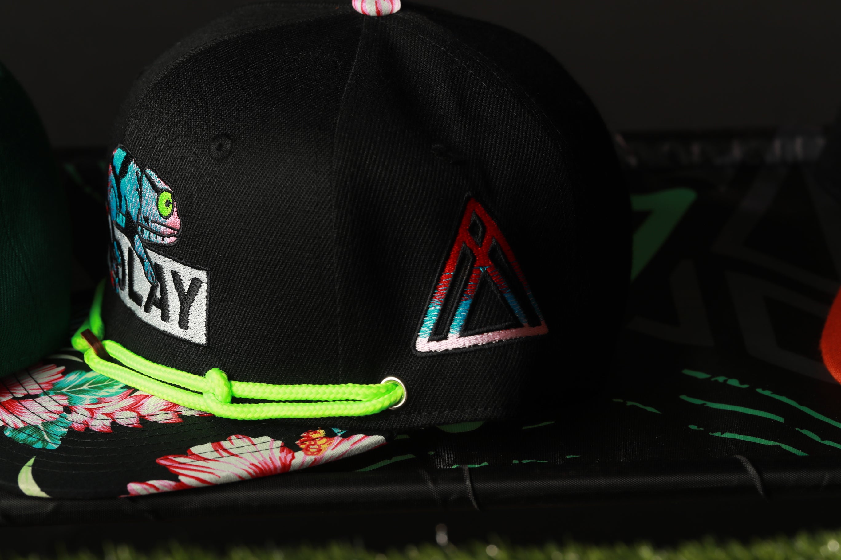 A black baseball cap with a colorful floral pattern and a red triangle logo on the front.