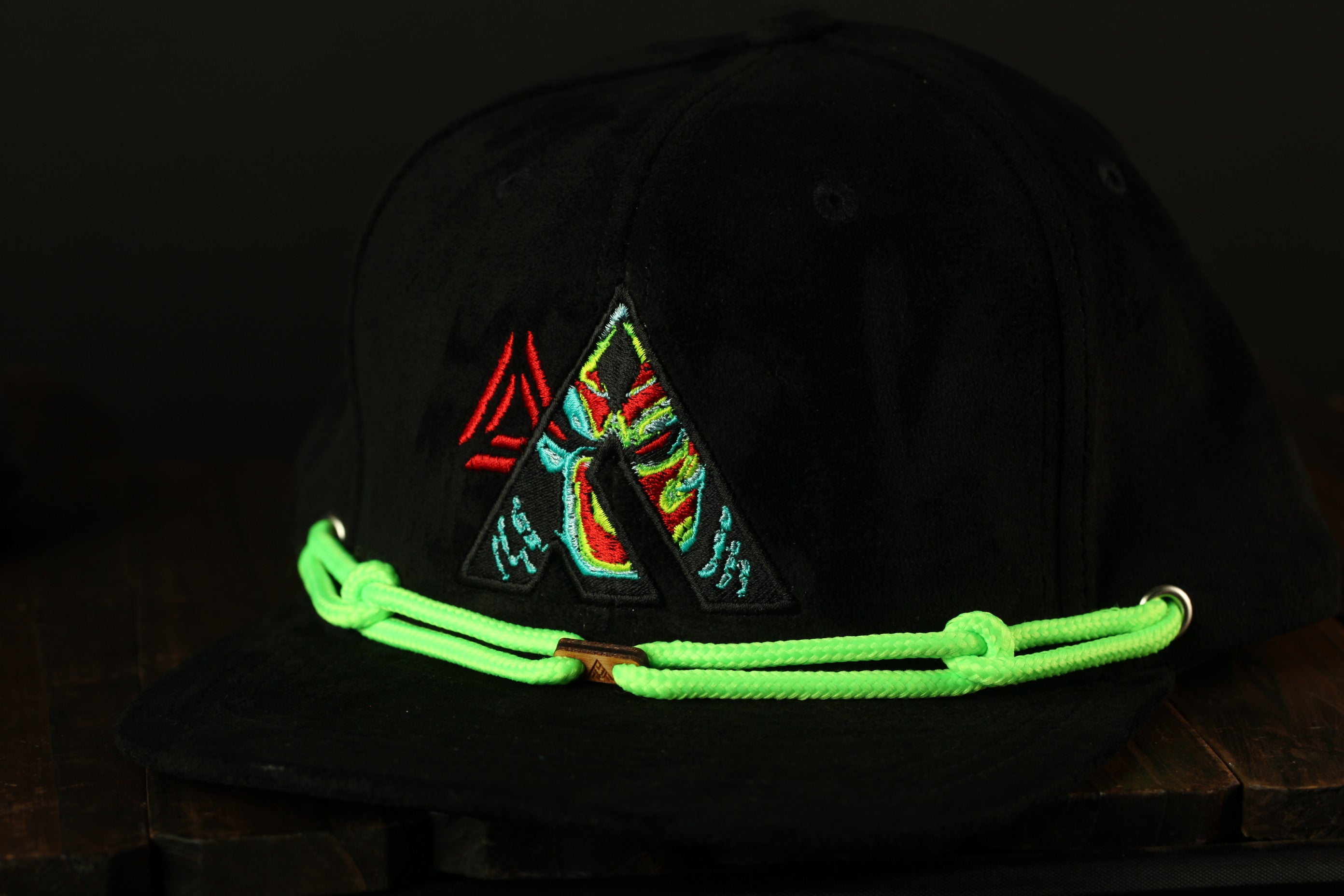 A black baseball cap with a colorful triangle-shaped logo and neon green strings.