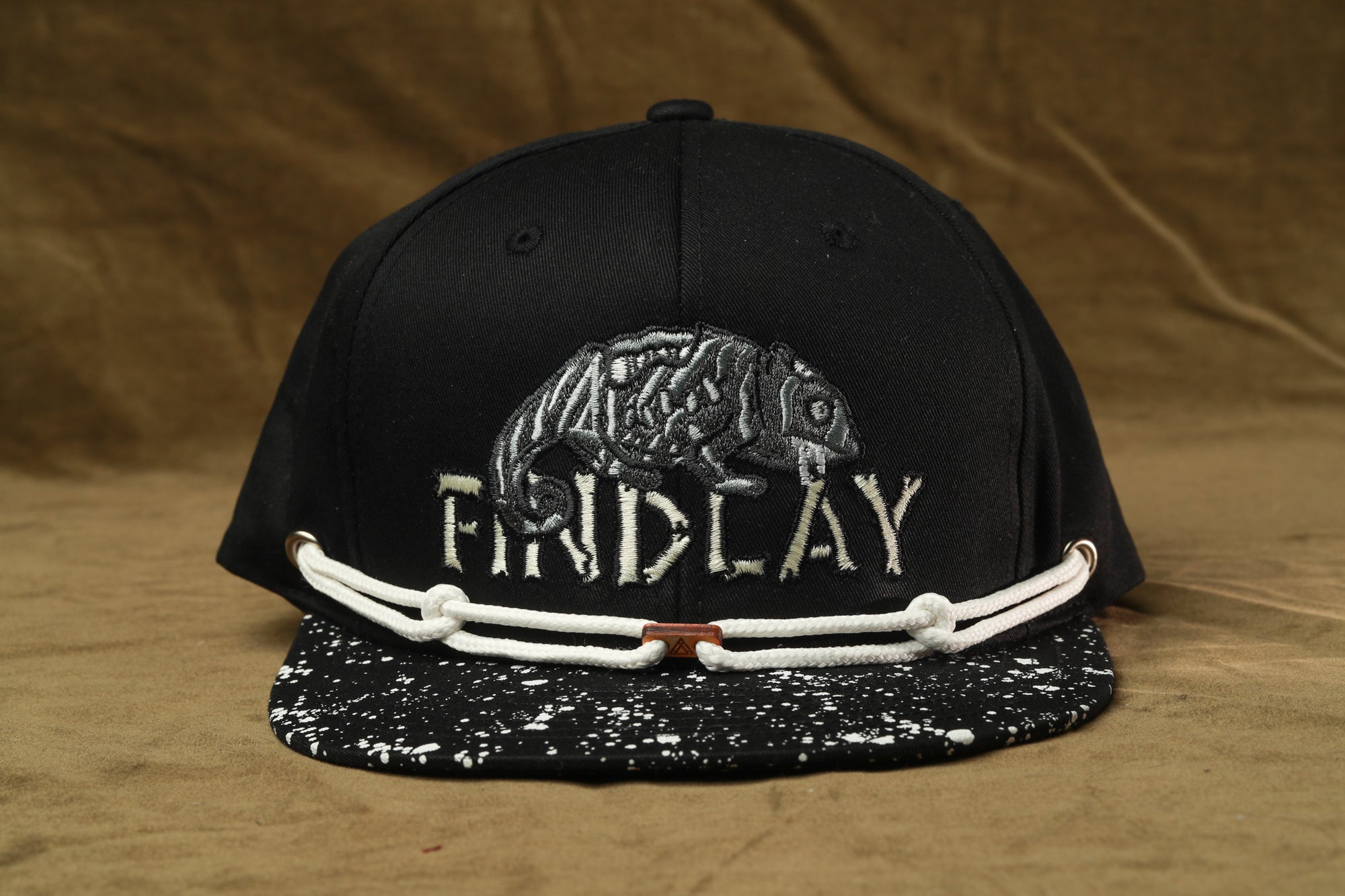 A black baseball cap with a white and black speckled pattern and the word "FINDlay" embroidered on it.
