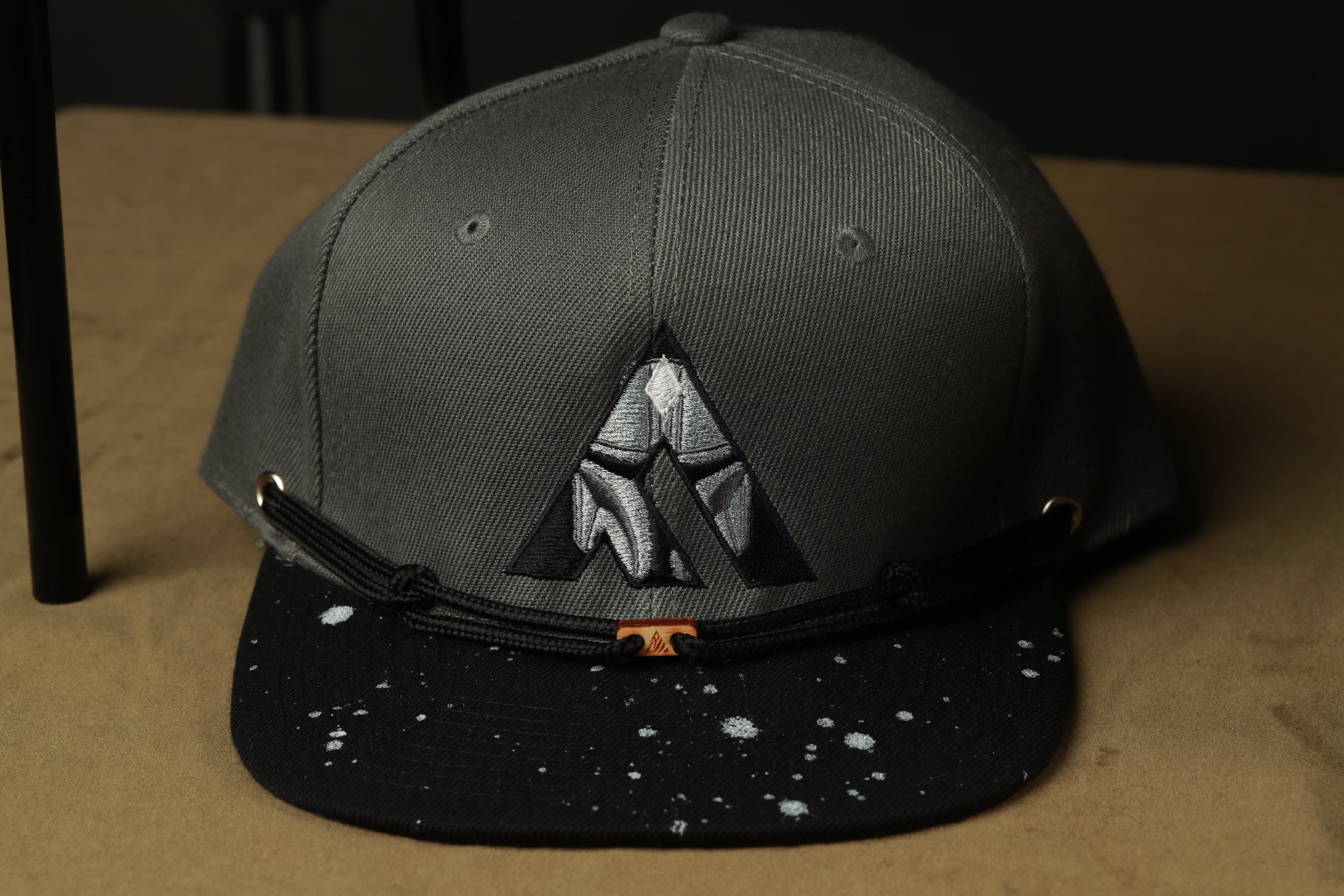 A gray baseball cap with a black brim and a black and white speckled pattern on the front.