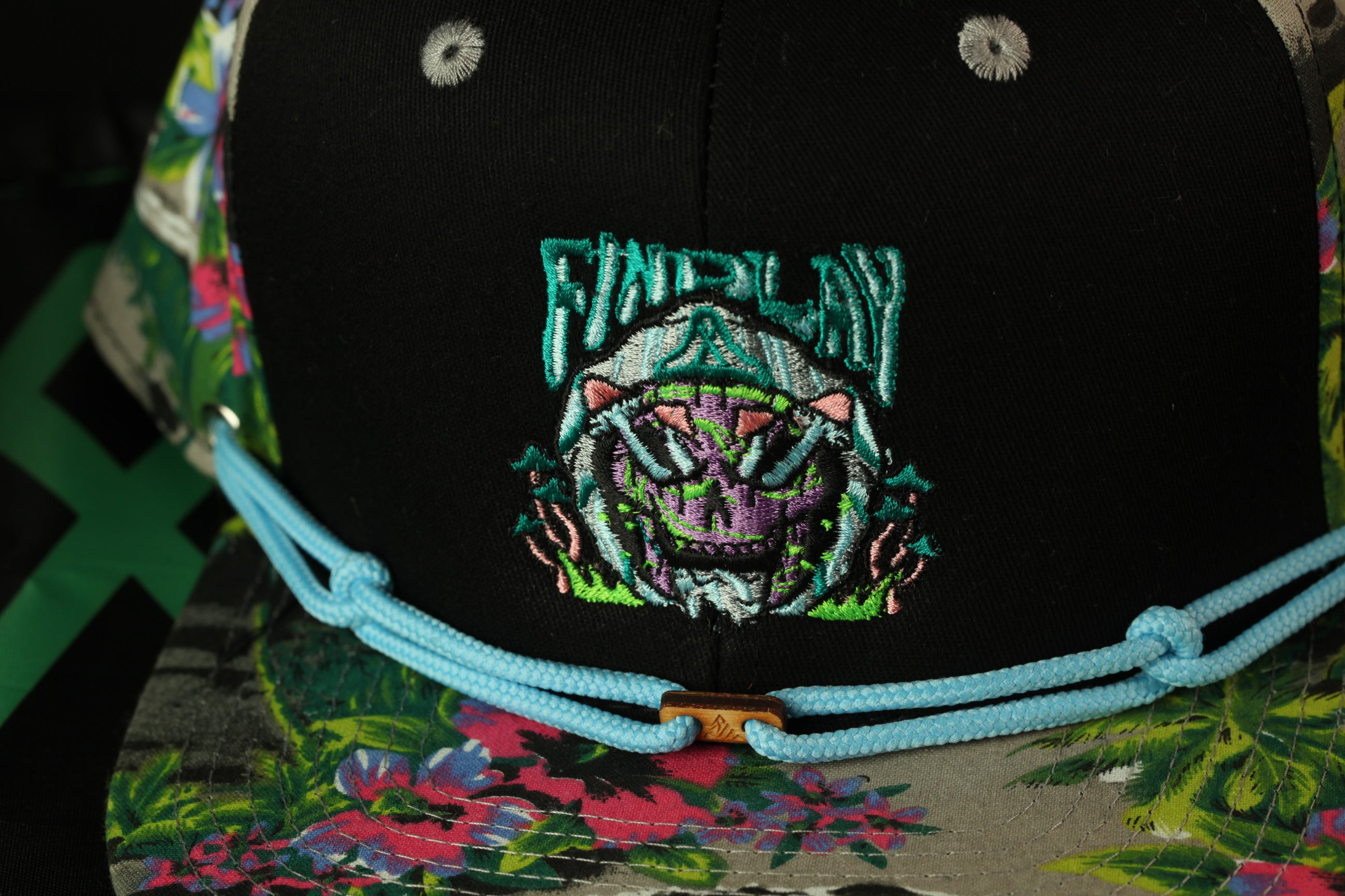 A close-up view of a black baseball cap with a colorful floral pattern and a skull-like embroidered design on the front.