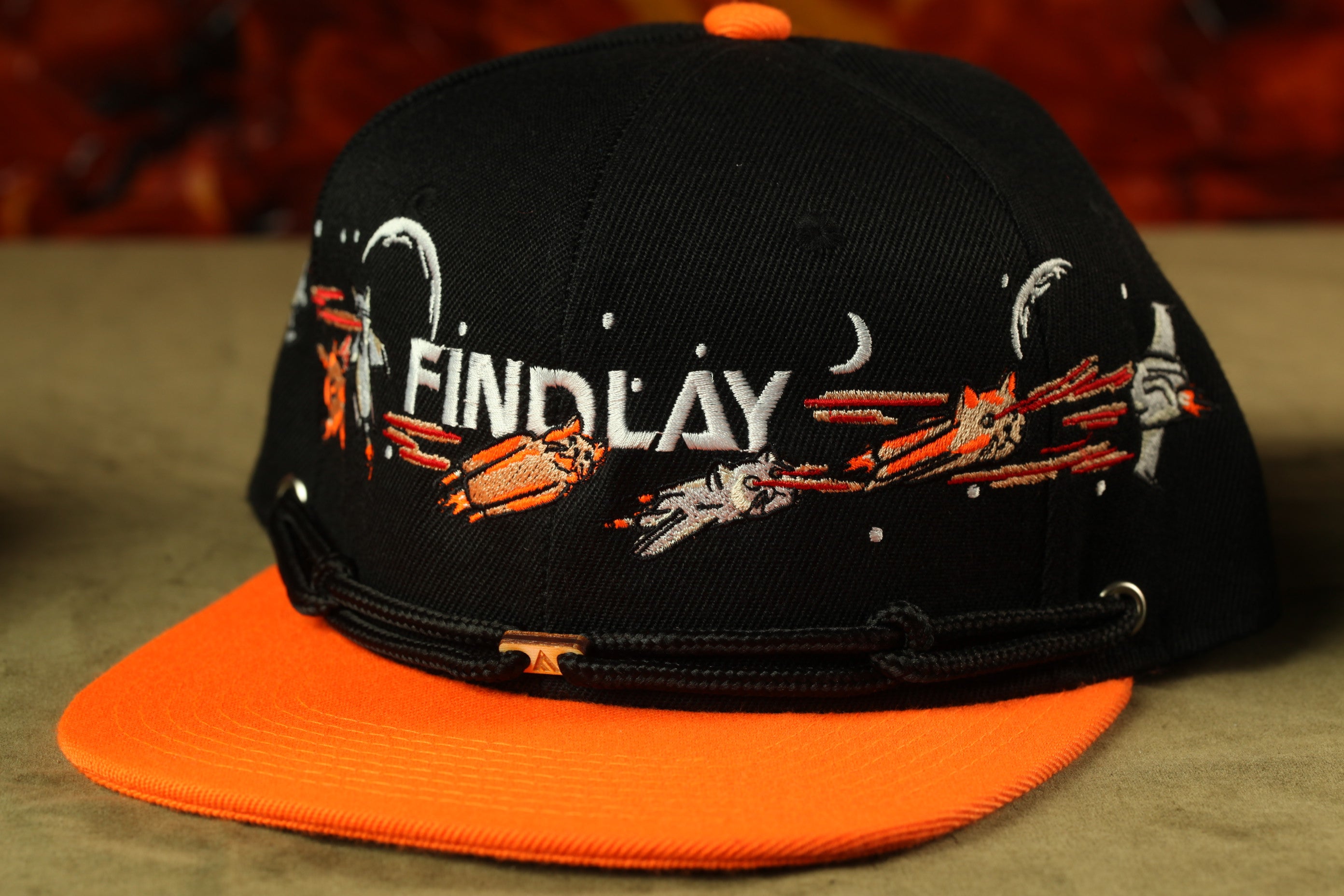 A black baseball cap with an orange brim, featuring a white and orange embroidered design and the word "FINDLAY" printed on it.