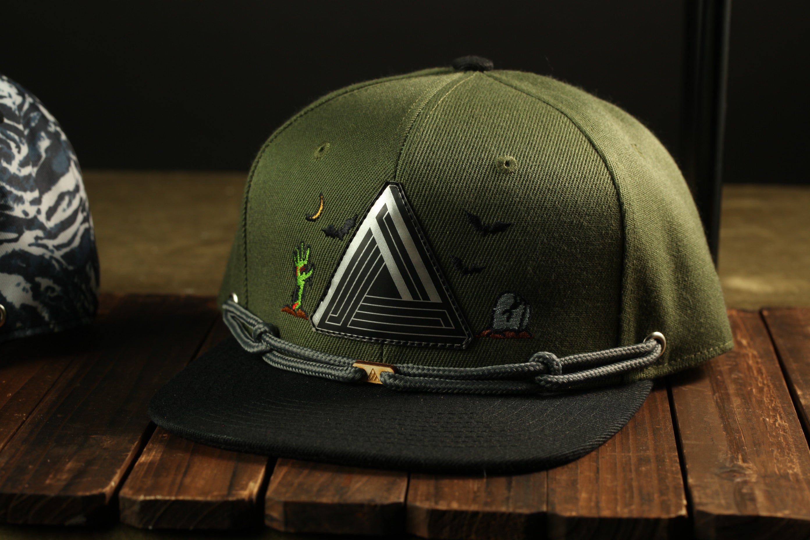 A green baseball cap with a geometric design and a black strap is displayed on a wooden surface.