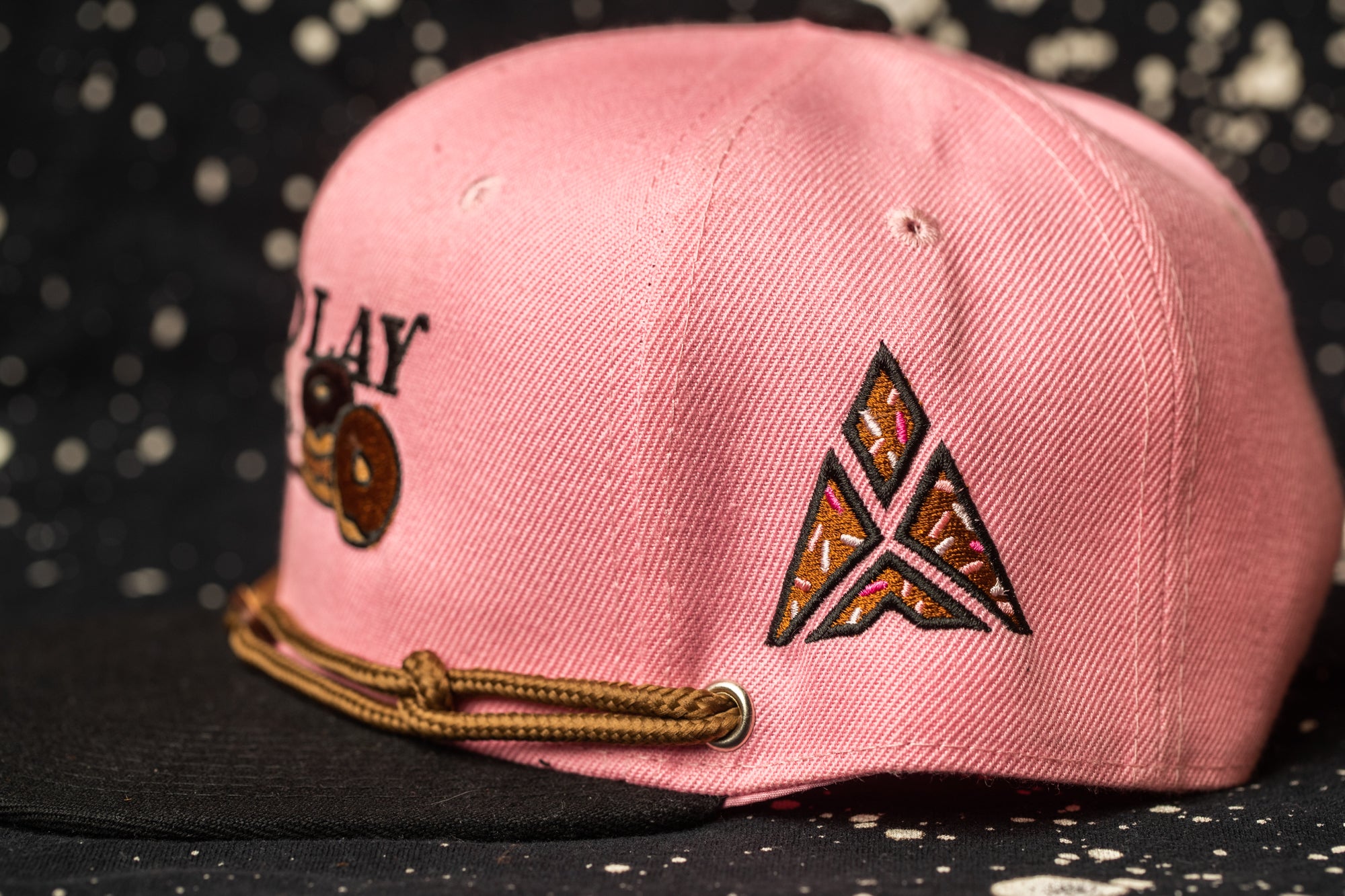 A pink baseball cap with a brown string and a triangle-shaped logo on the front.
