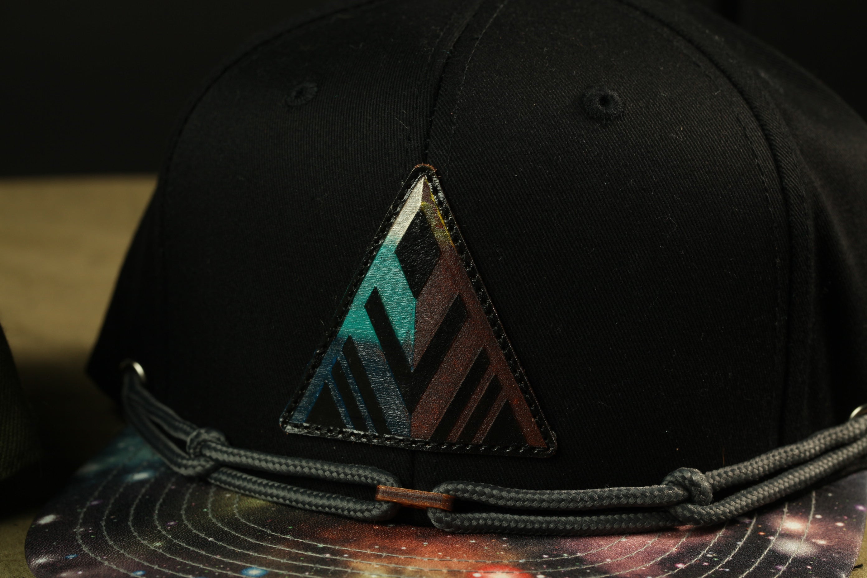 A close-up view of a black baseball cap with a colorful triangular patch on the front.