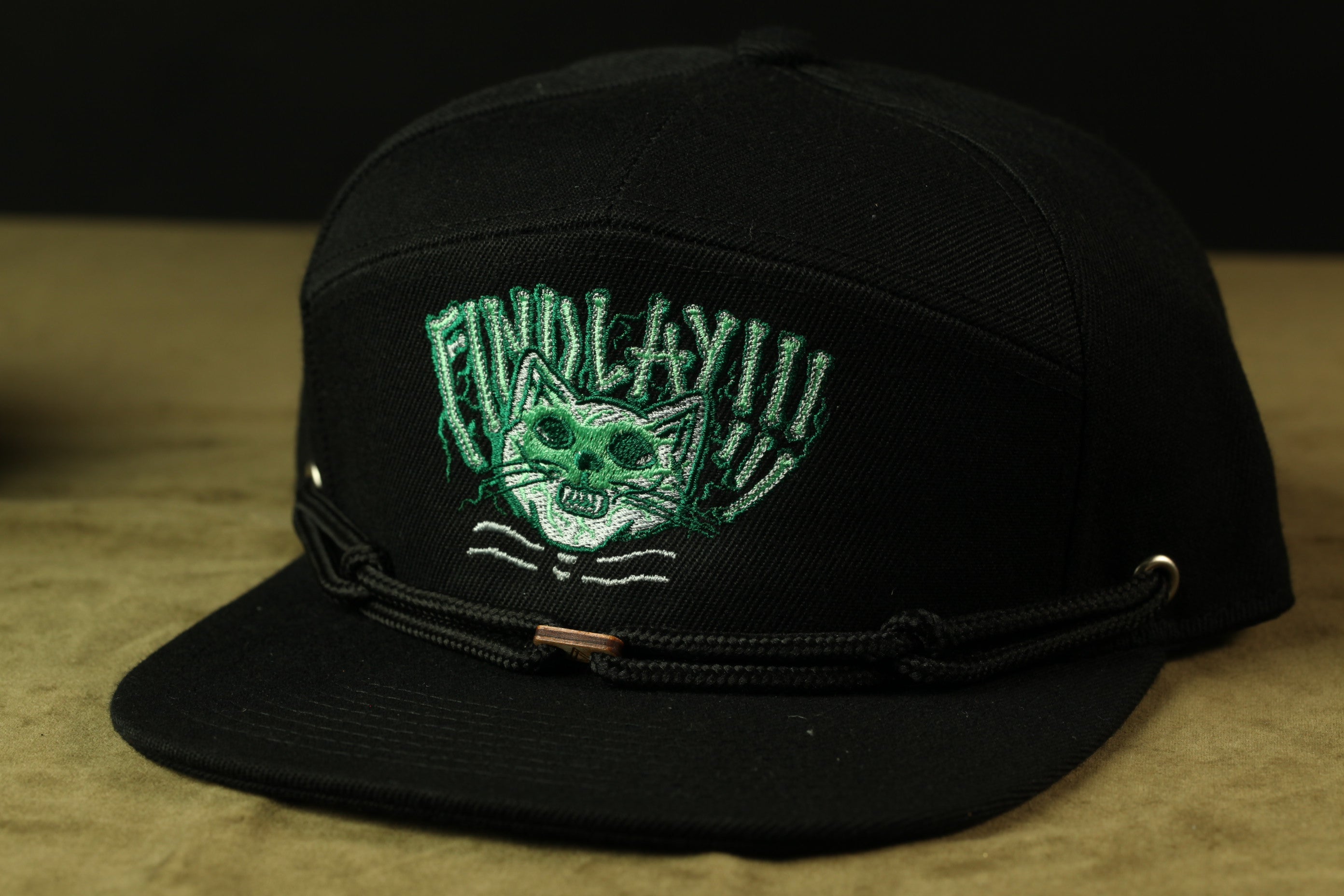 A black baseball cap with a green cat embroidered on it.