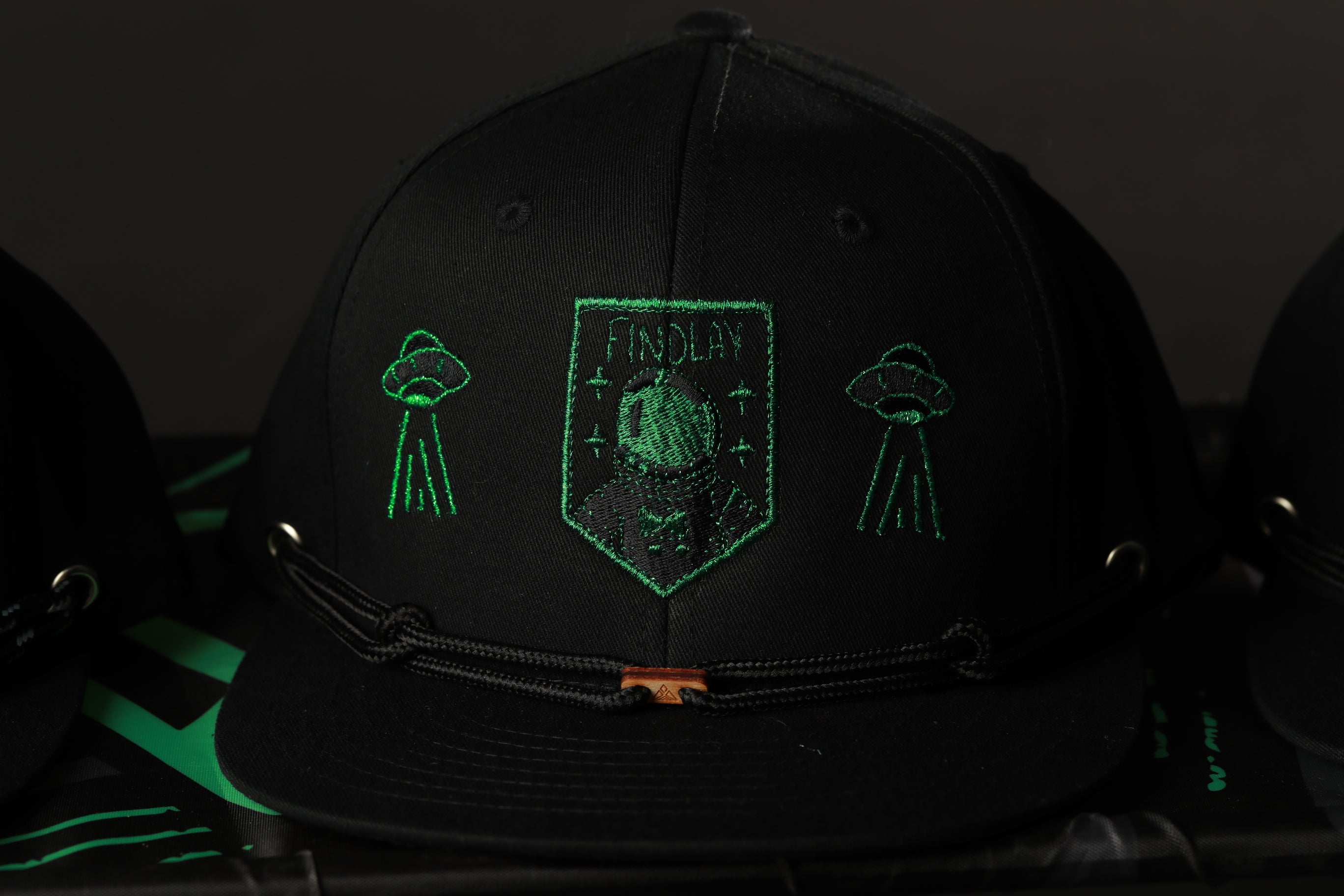 A black baseball cap with green embroidered designs and text.