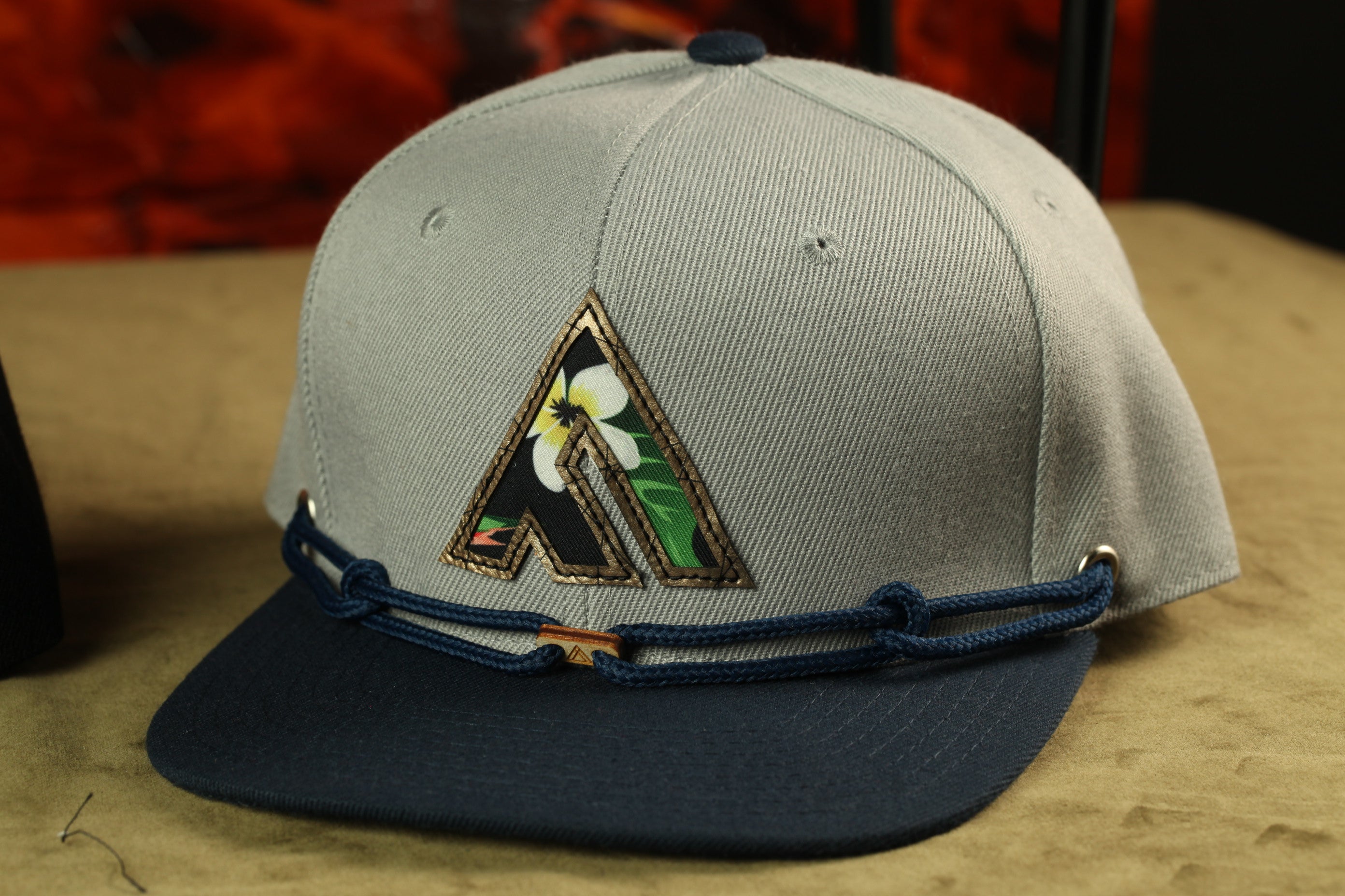 A gray baseball cap with a floral logo on the front, sitting on a brown surface.