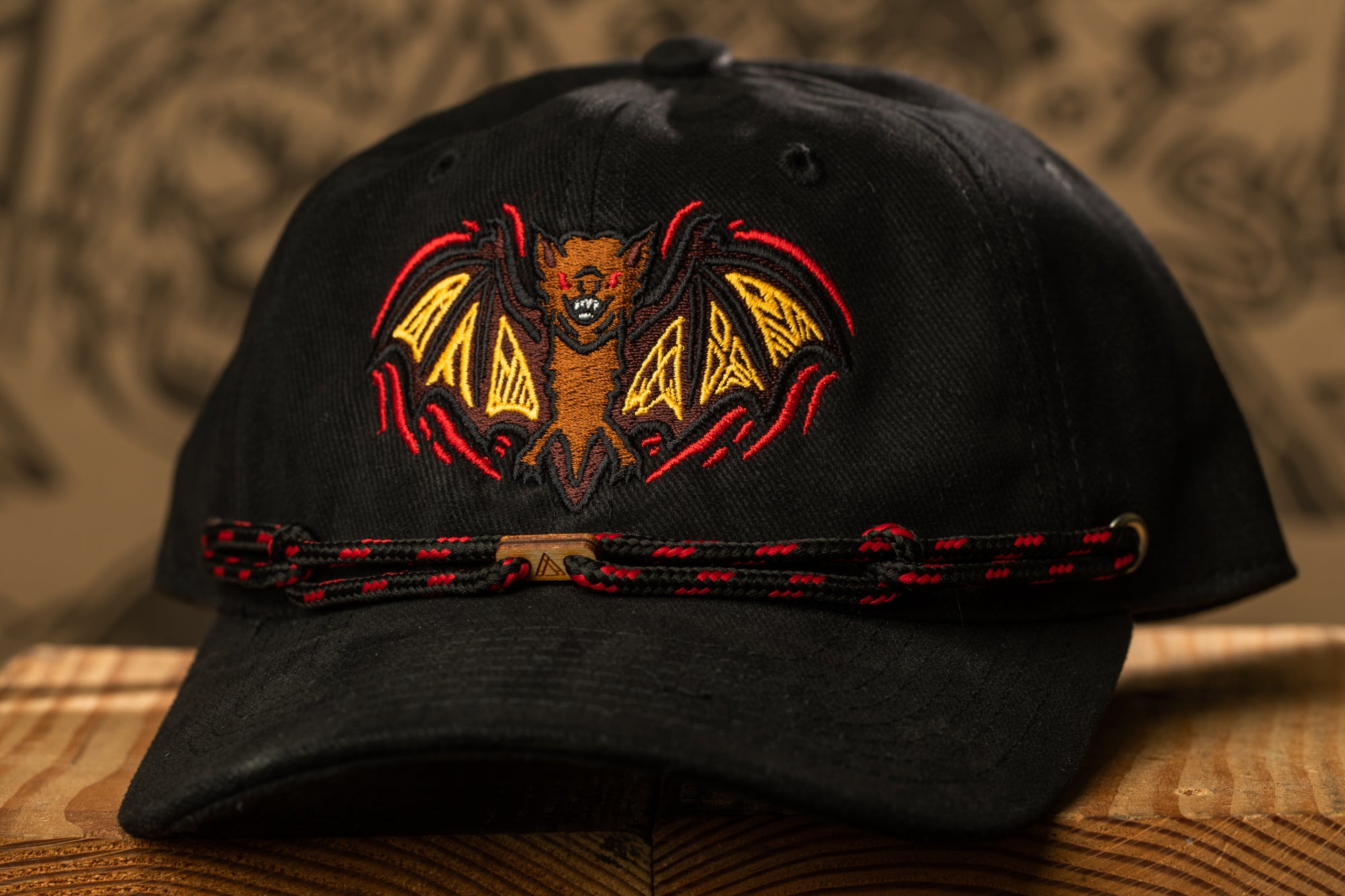 A black baseball cap with a bat embroidered on it, featuring a red and yellow bat design.