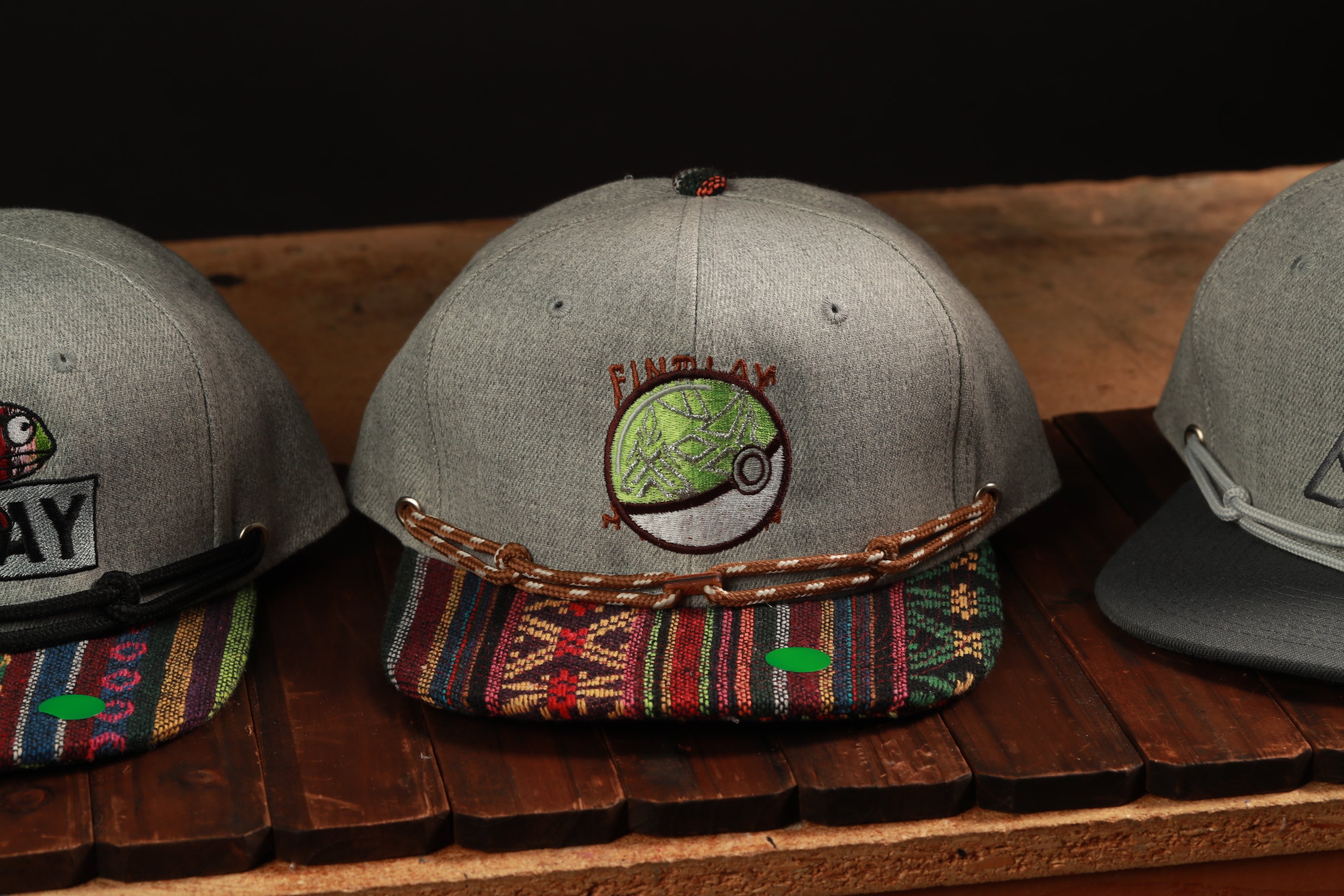 Three baseball caps are displayed on a wooden surface, with one featuring a Pokemon logo.