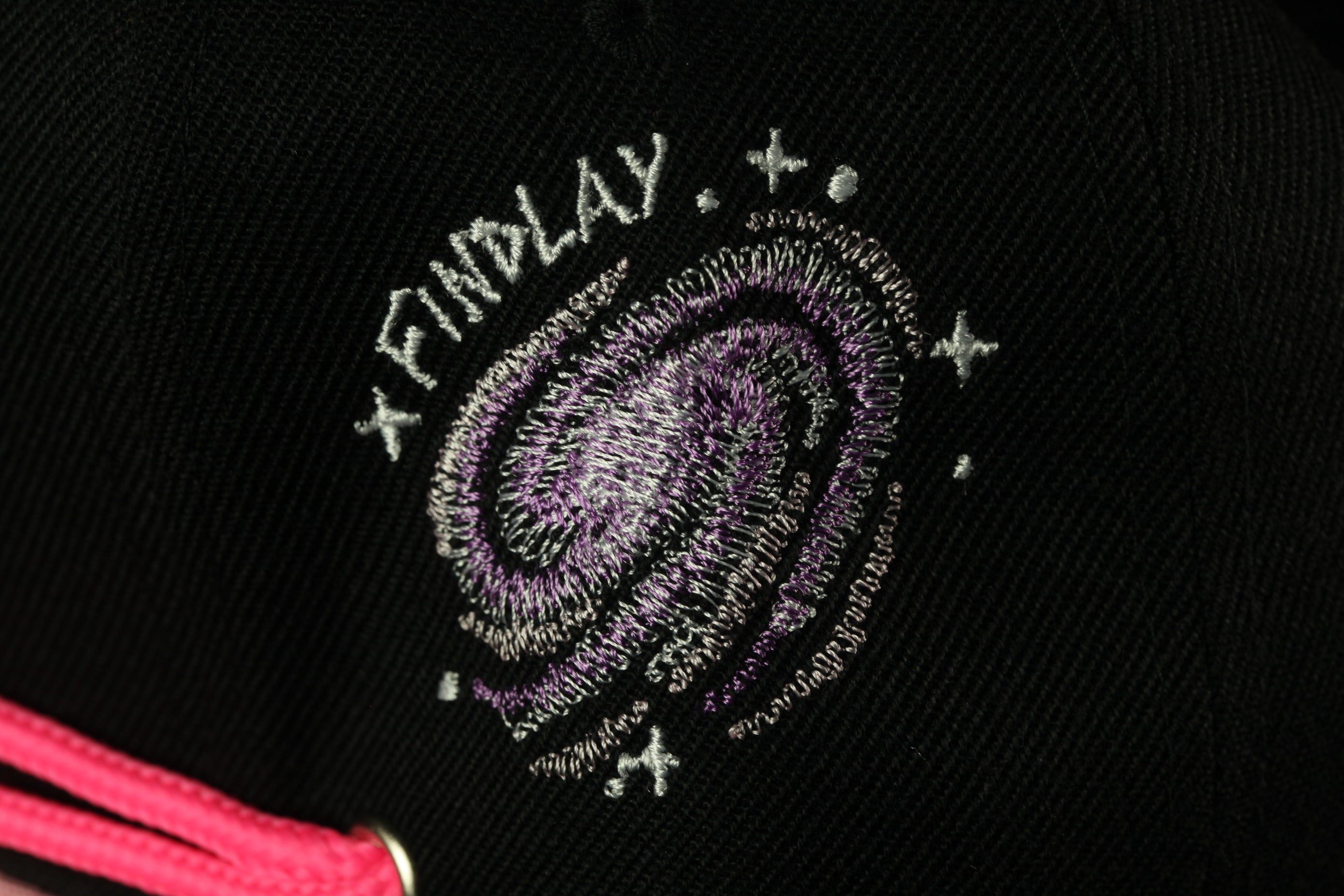 a close-up view of a black fabric with a purple and white embroidered design featuring a spiral galaxy and stars.