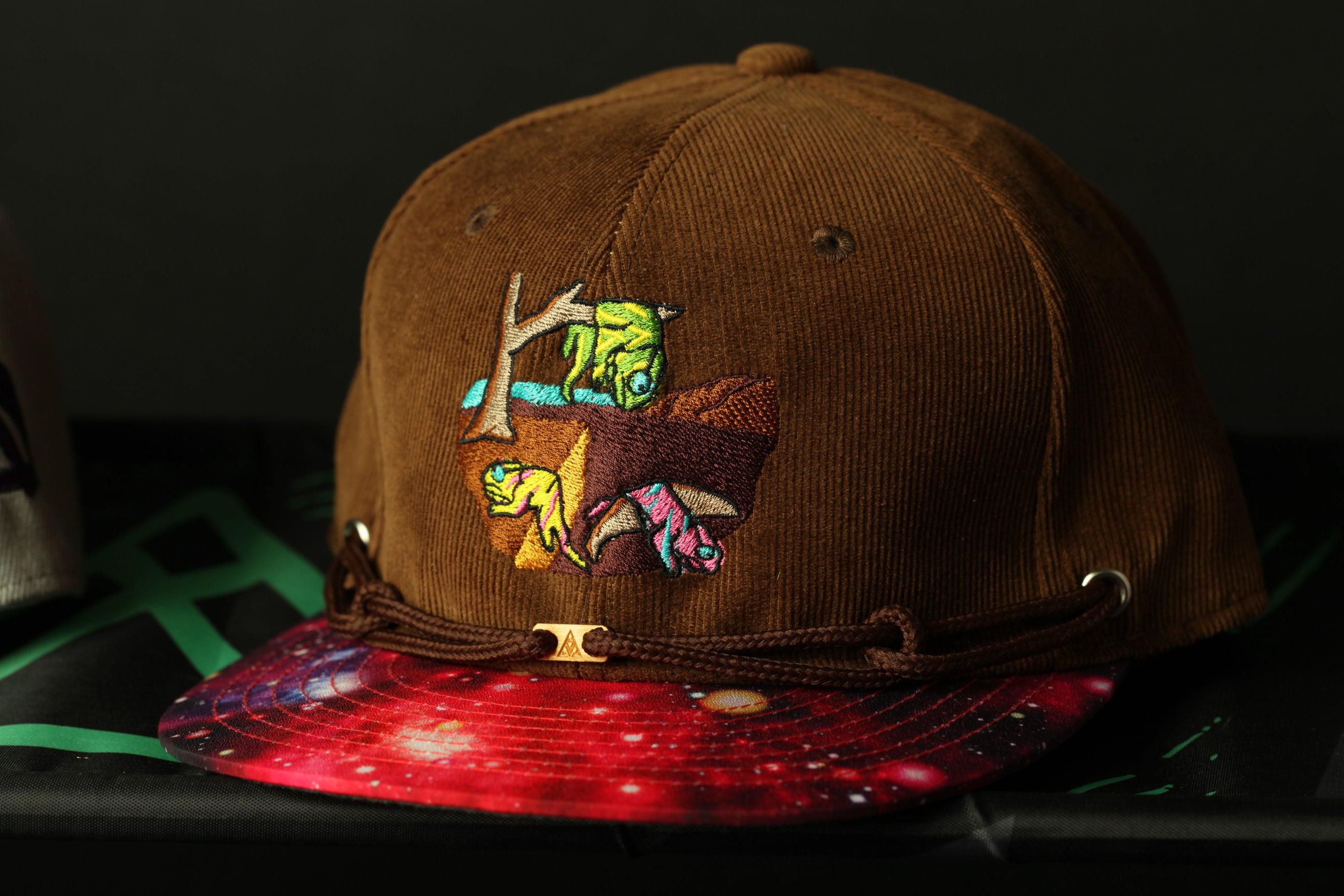 A brown baseball cap with a colorful embroidered design on the front, featuring a small animal and a tree.