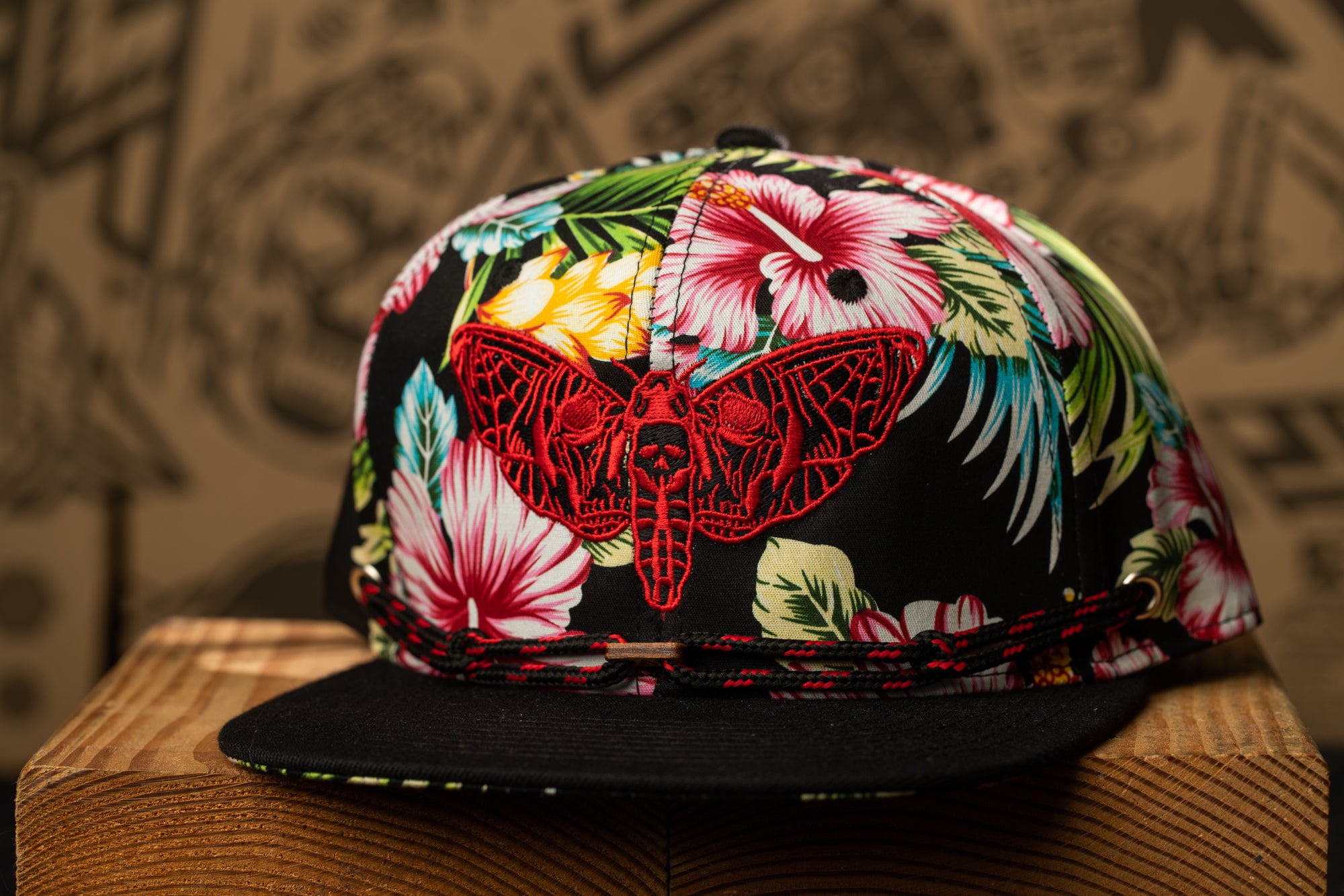 A colorful floral-patterned baseball cap with a red butterfly design on the front, resting on a wooden surface.