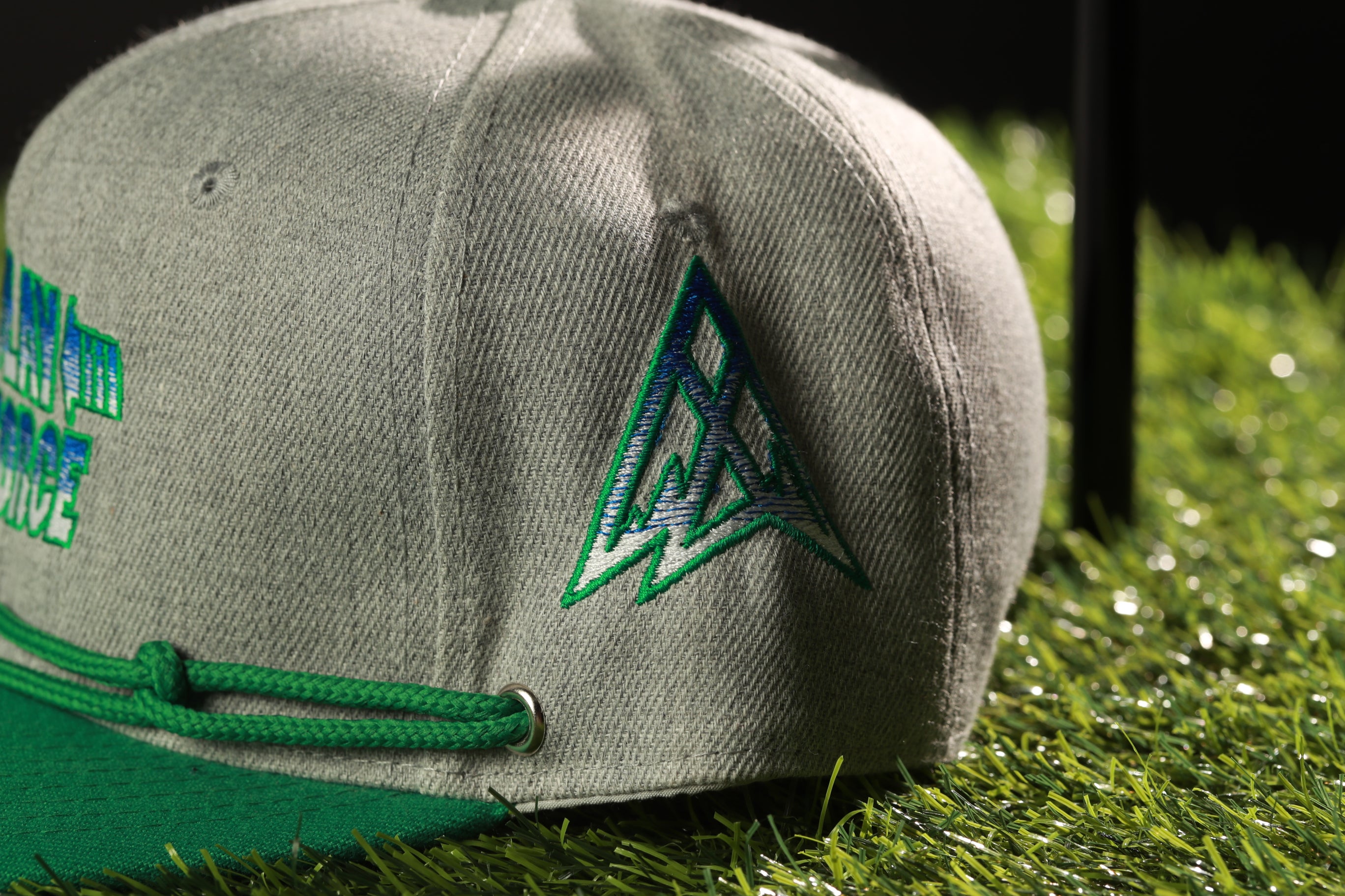 A gray baseball cap with a green brim and a logo on the side, placed on a grassy surface.