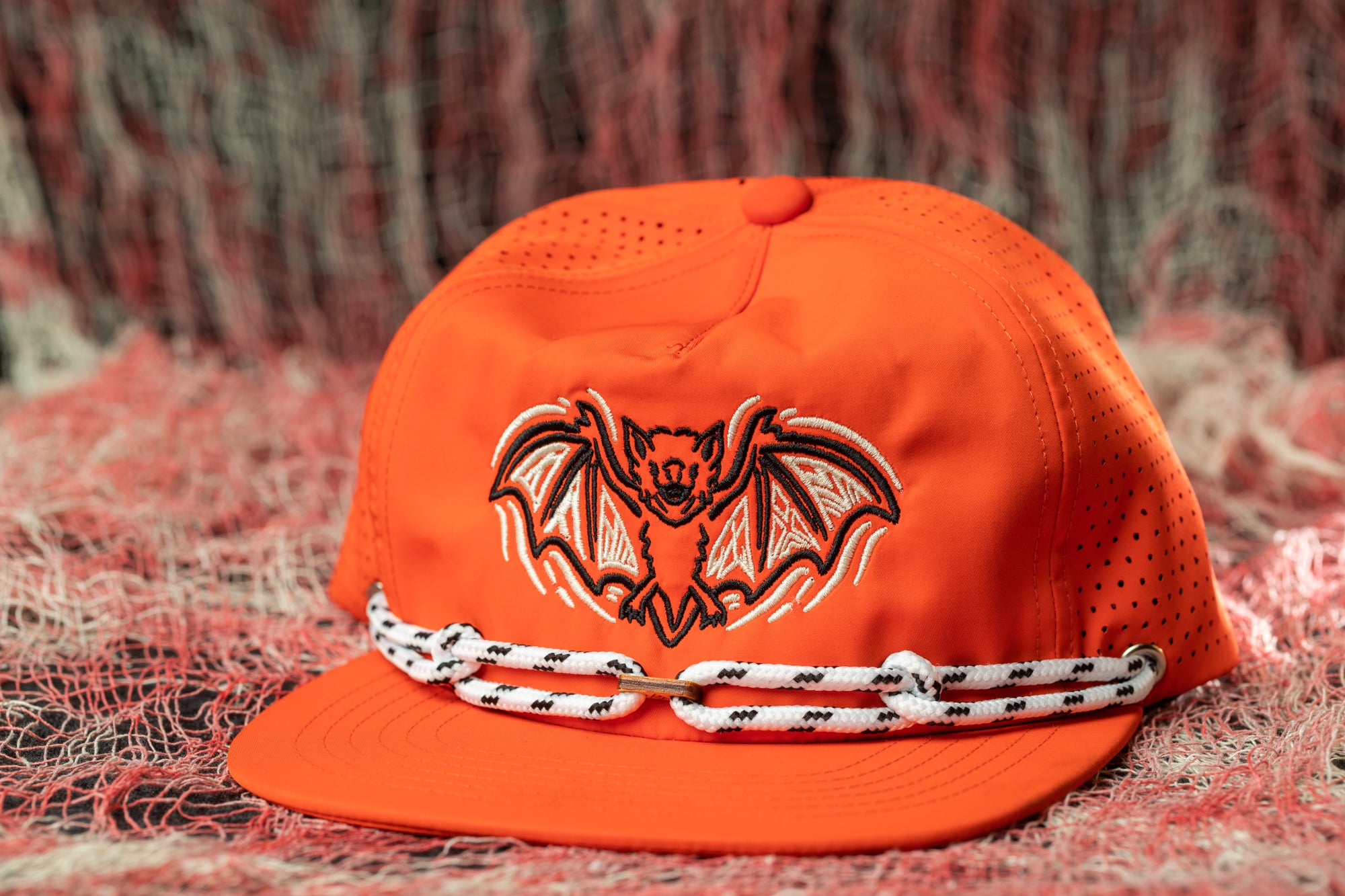 An orange baseball cap with a bat design on it, placed on a red and white background.