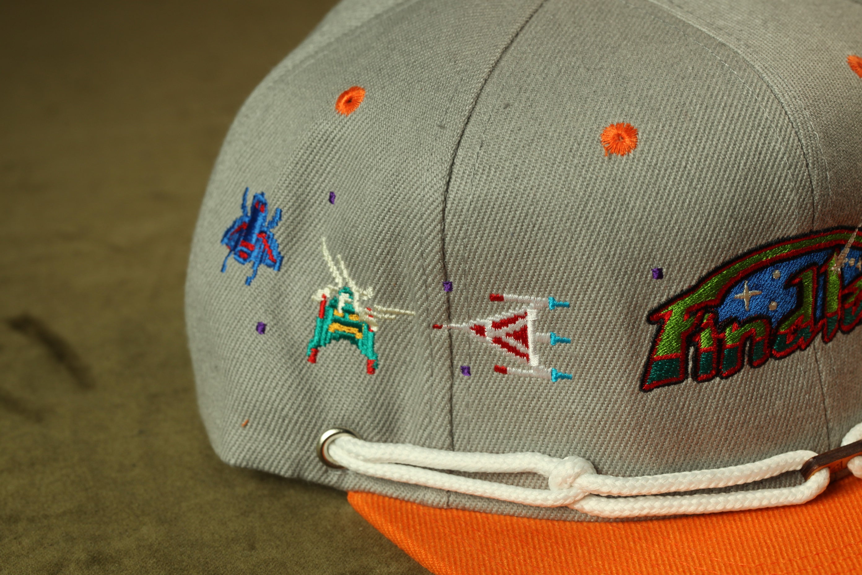 a gray baseball cap with various colorful embroidered designs, including a small insect, a star, and a flag.