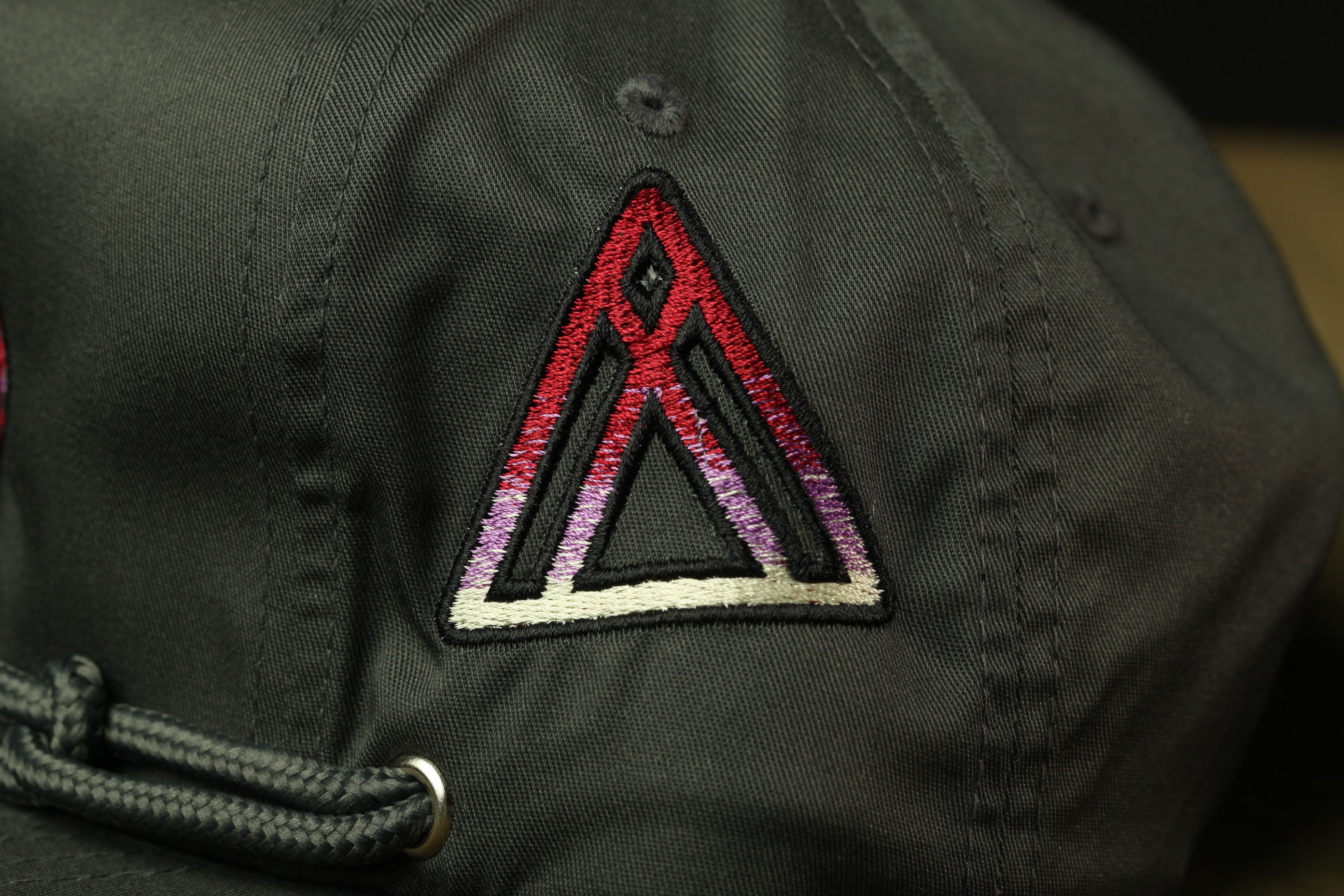 A close-up view of a black baseball cap with a red and white triangle embroidered on the front.