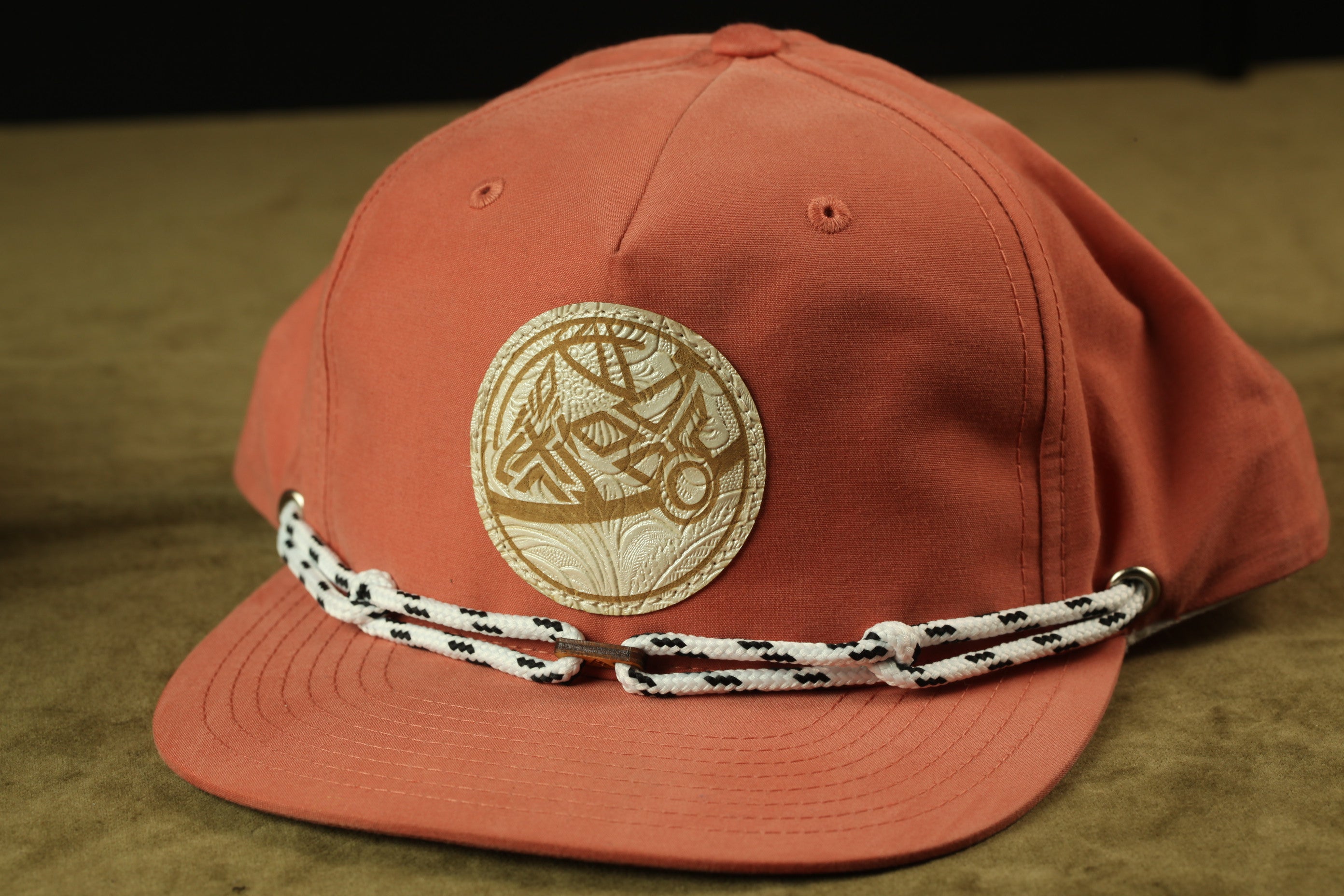 A red baseball cap with a white and gold embroidered logo on the front, and a black and white braided strap.