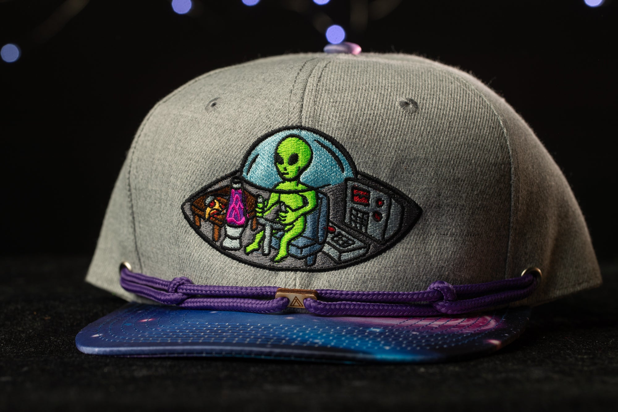 A gray baseball cap with a colorful alien embroidered on it, featuring a space-themed design.