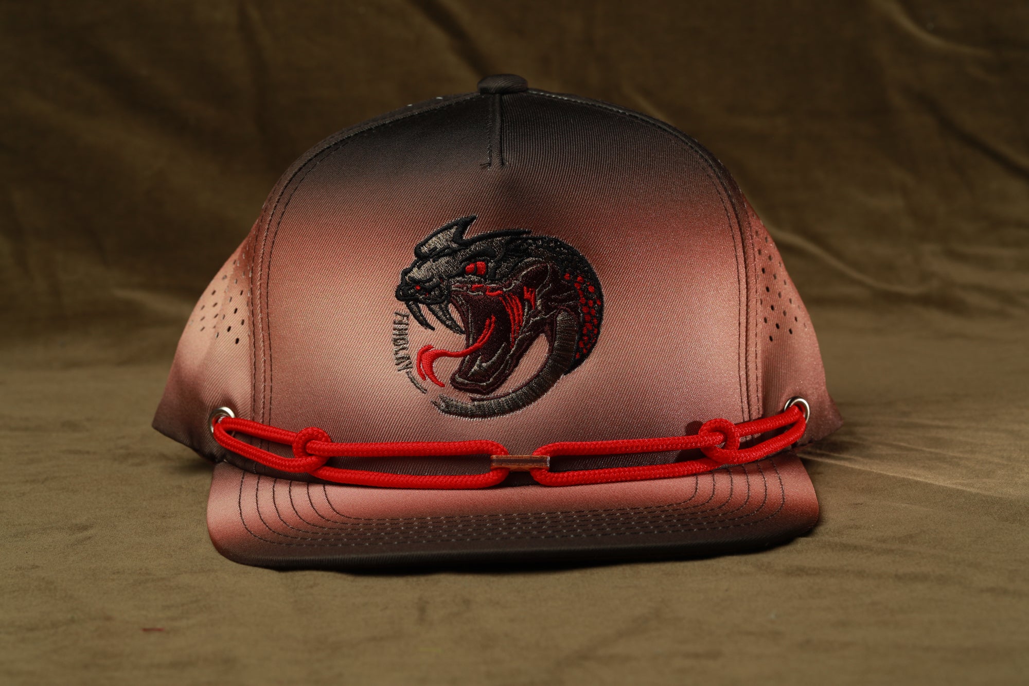 A brown baseball cap with a red chain strap and a black and red snake design on the front.